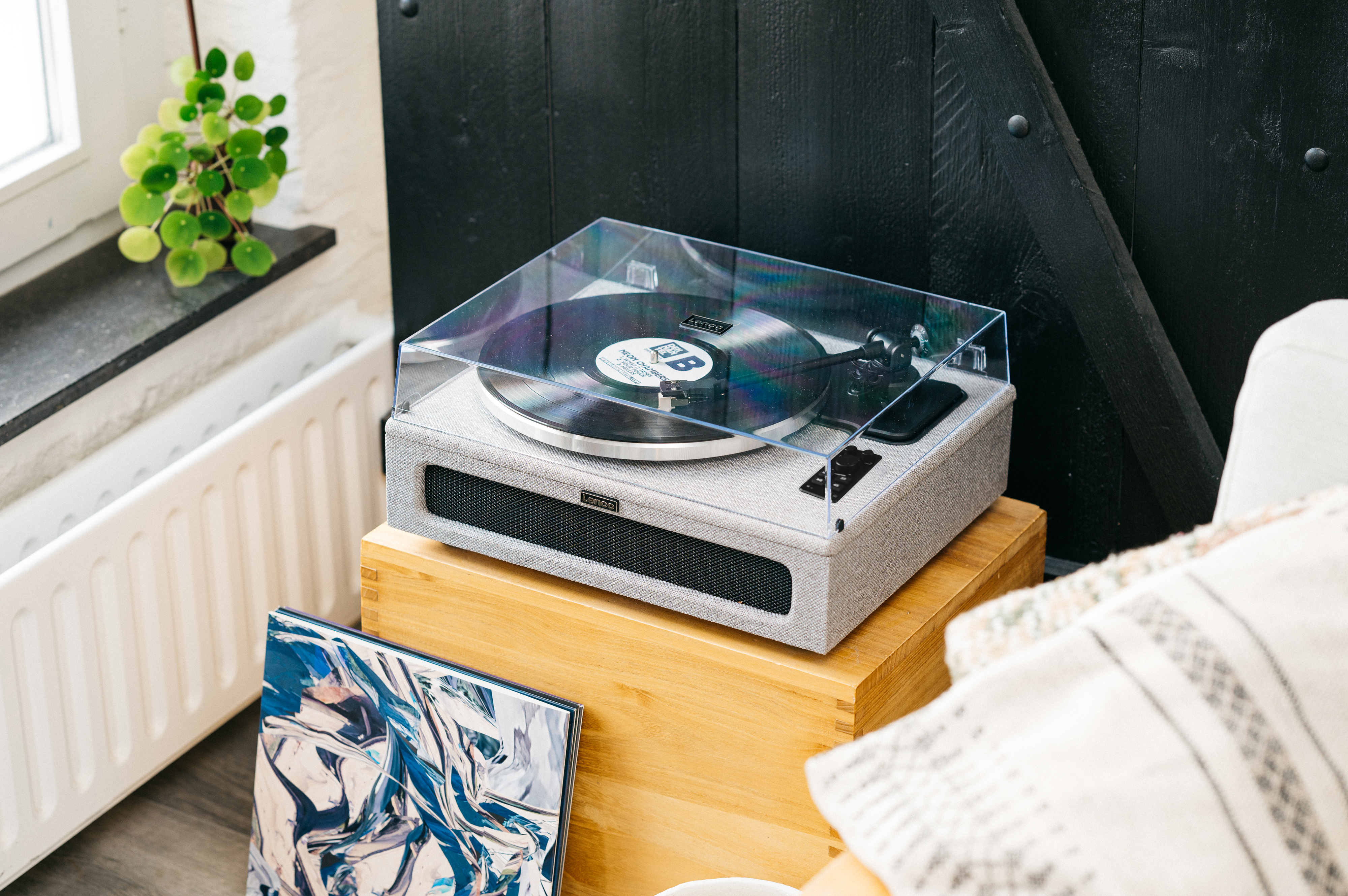 Un tocadiscos en un soporte de madera con una cubierta transparente. Otros artículos incluyen un disco y almohadas.
