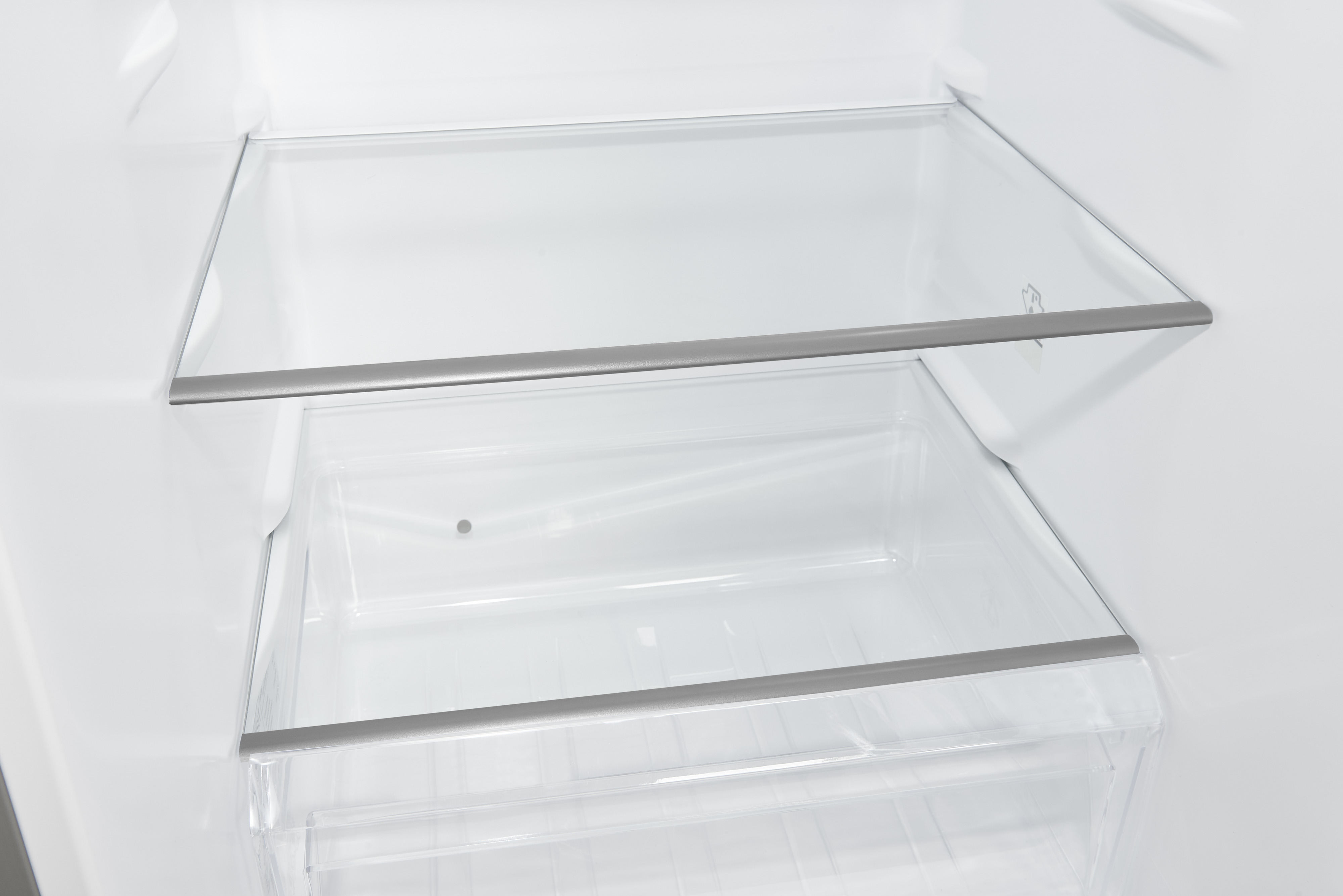 Innenraum eines Kühlschranks mit Glasböden und einer durchsichtigen Plastikschublade.