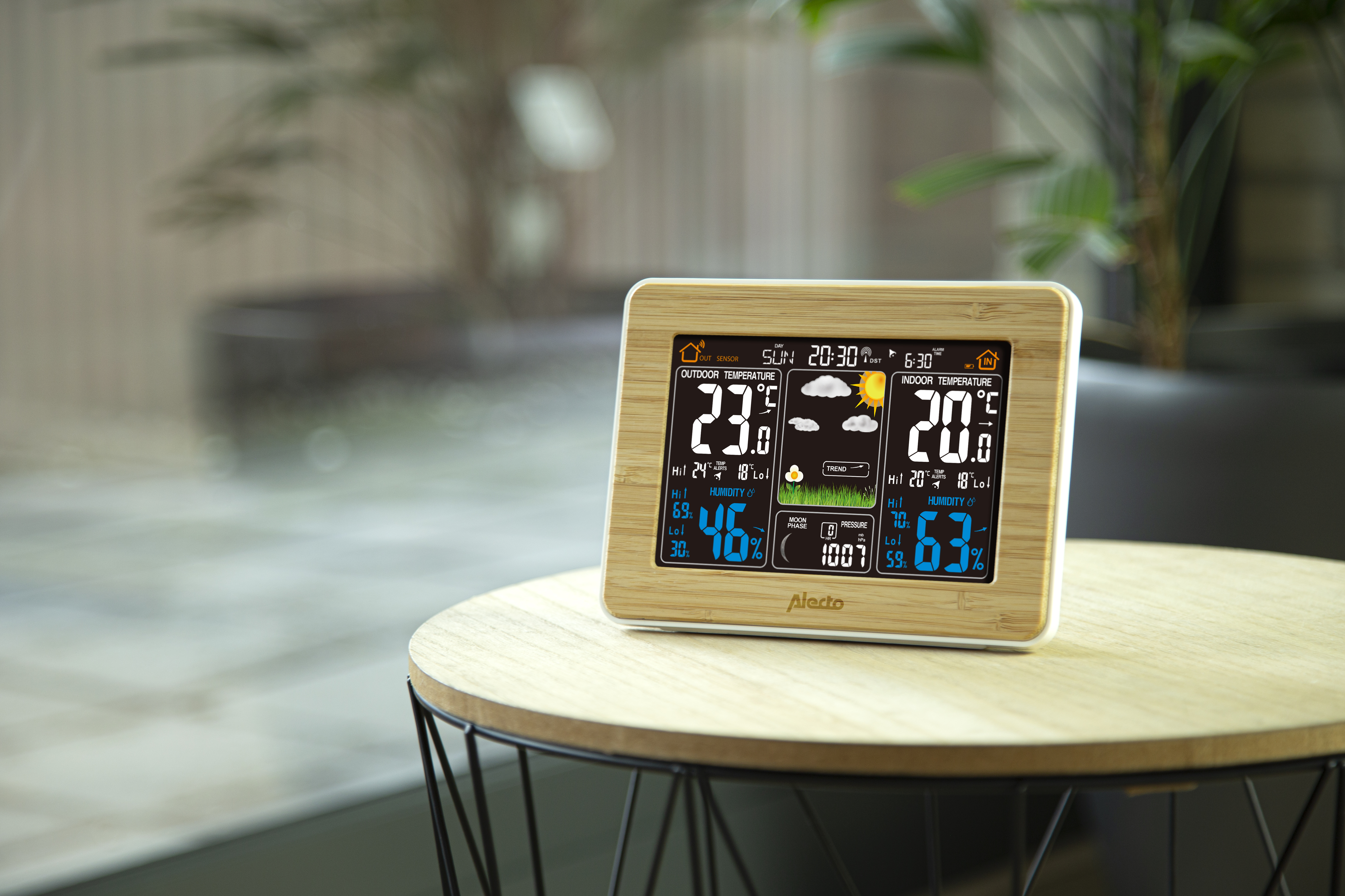 Eine digitale Wetterstation zeigt Innen-/Außentemperatur, Luftfeuchtigkeit und Zeit auf einem Tisch an.