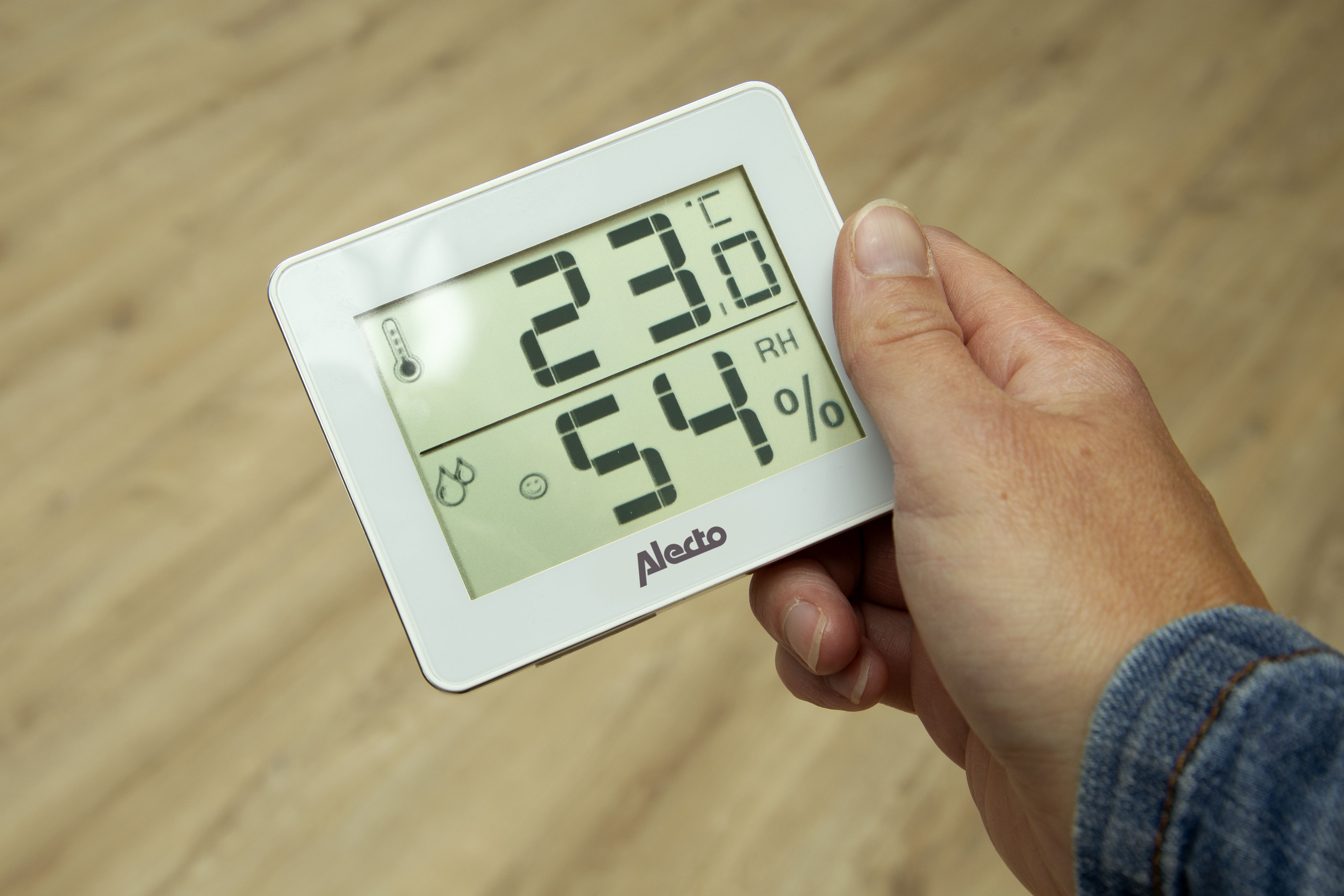 Hand hält ein weißes digitales Thermometer, das Temperatur und Luftfeuchtigkeit anzeigt.