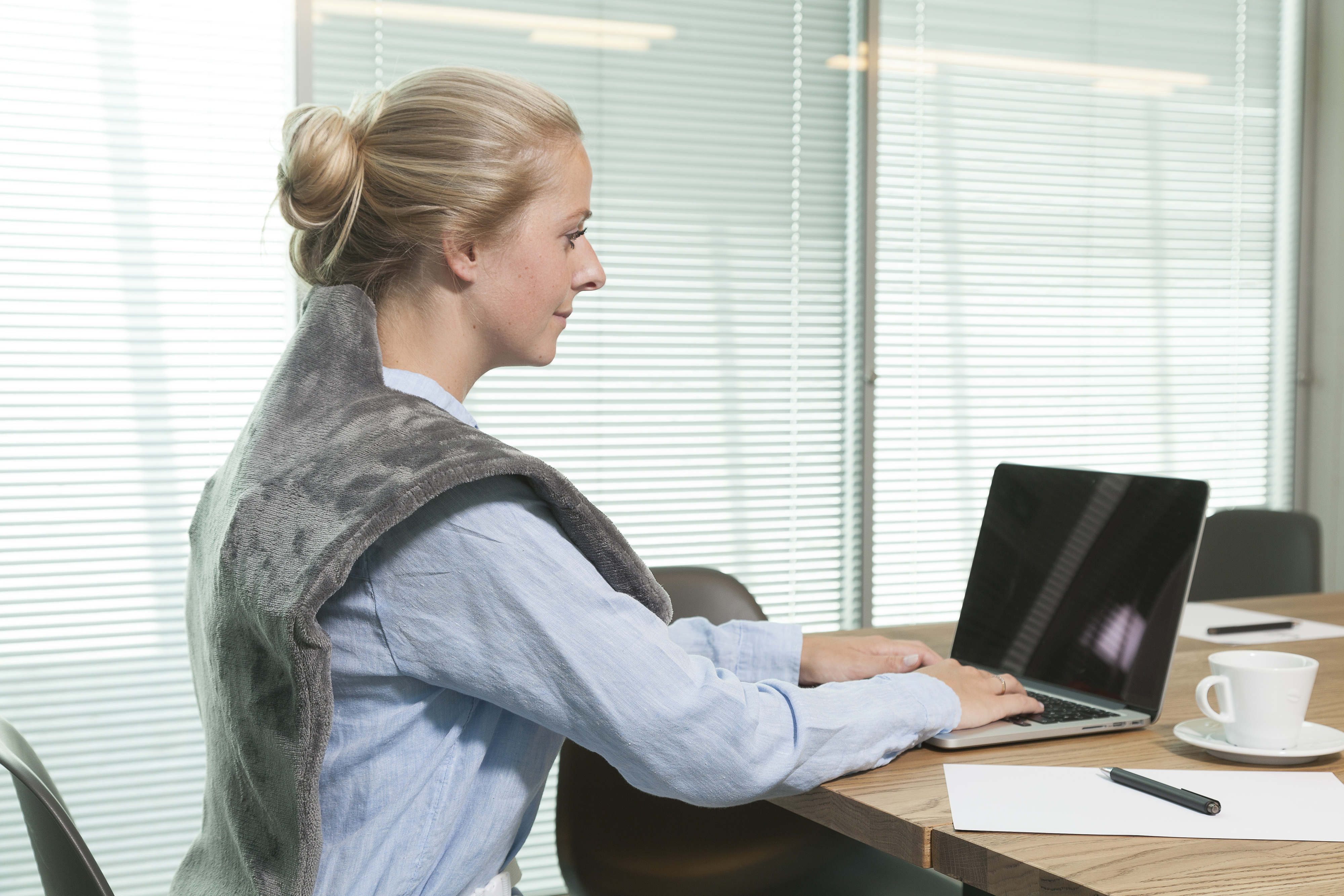 Donna con fascia grigia sul collo, che digita su un laptop a un tavolo riunioni.
