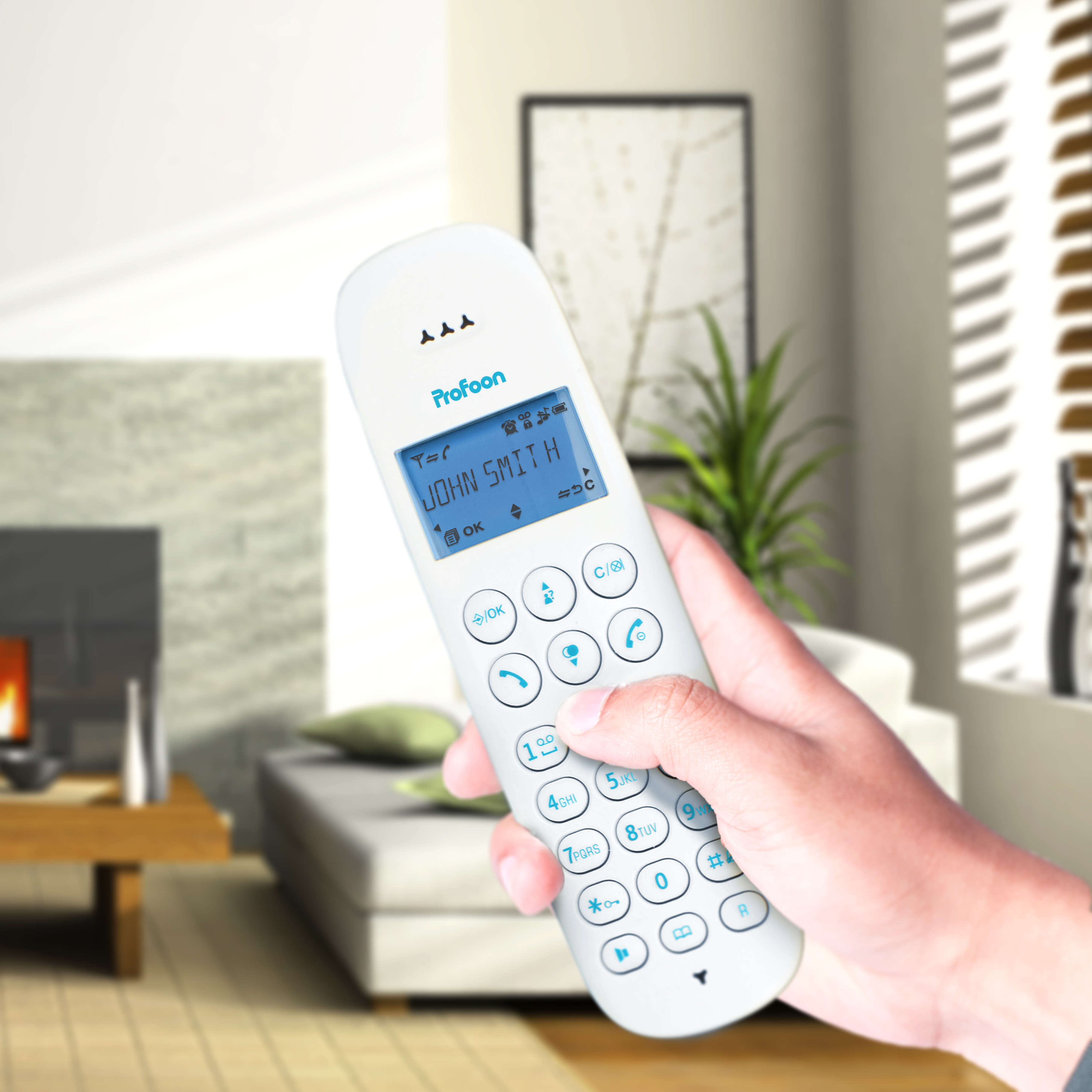 Una persona tiene in mano un telefono cordless bianco con display. Lo sfondo è un interno domestico.