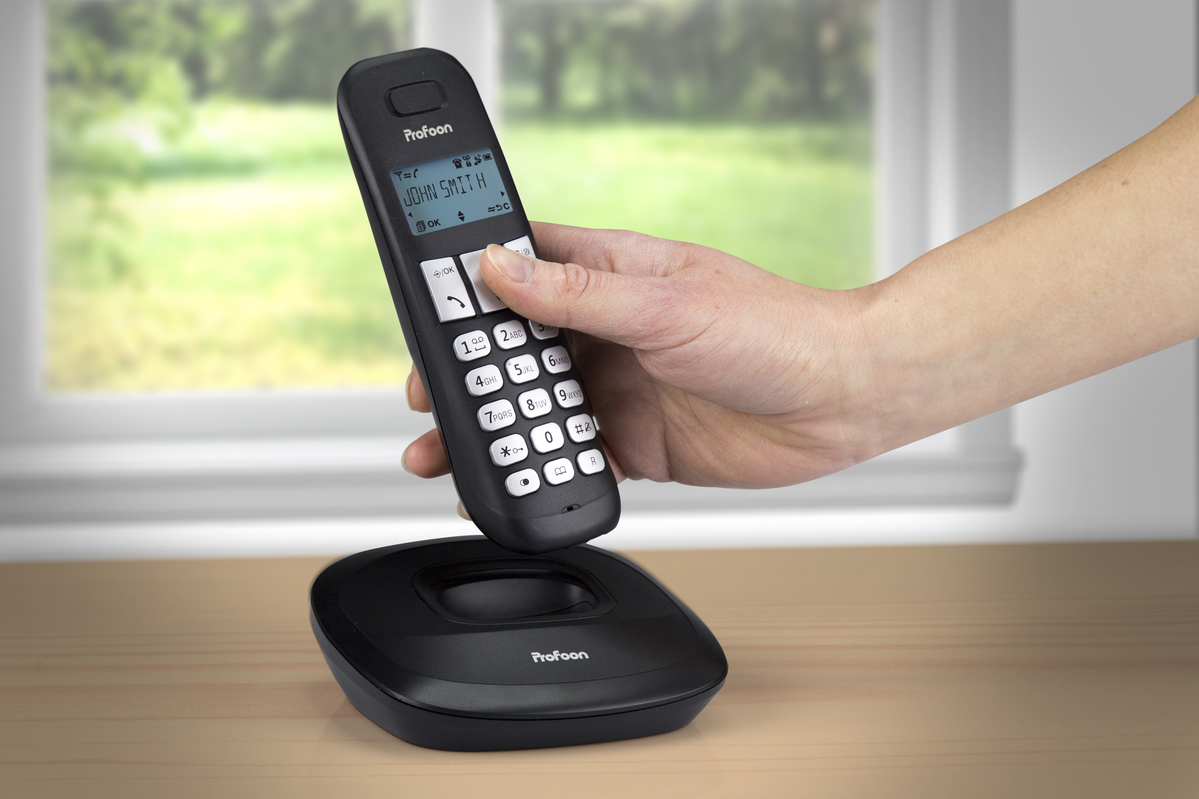 Eine Hand, die ein schnurloses Telefon über seiner Ladestation hält.