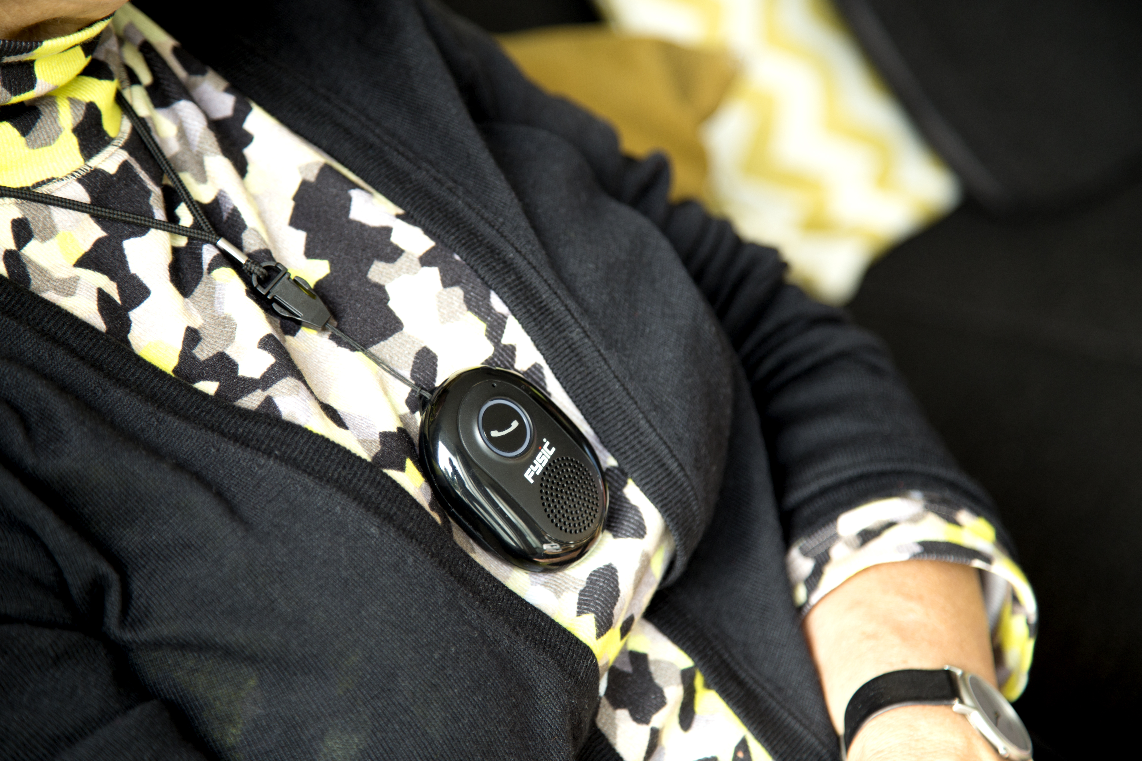 A woman wears a black pendant with a black communication button. She wears a black jacket.