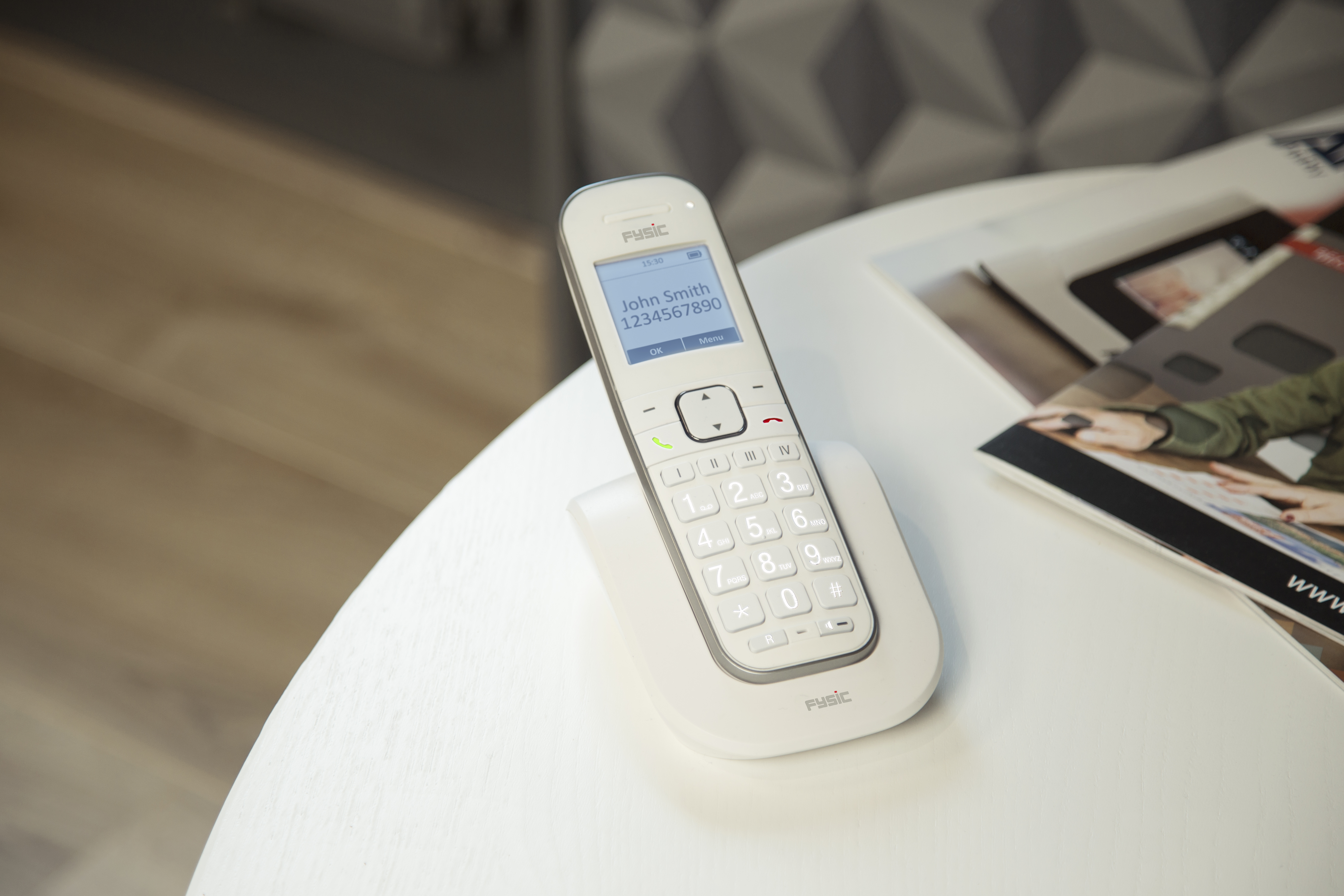 Ein weißes schnurloses Telefon liegt auf einer weißen Basis auf einem weißen Tisch.