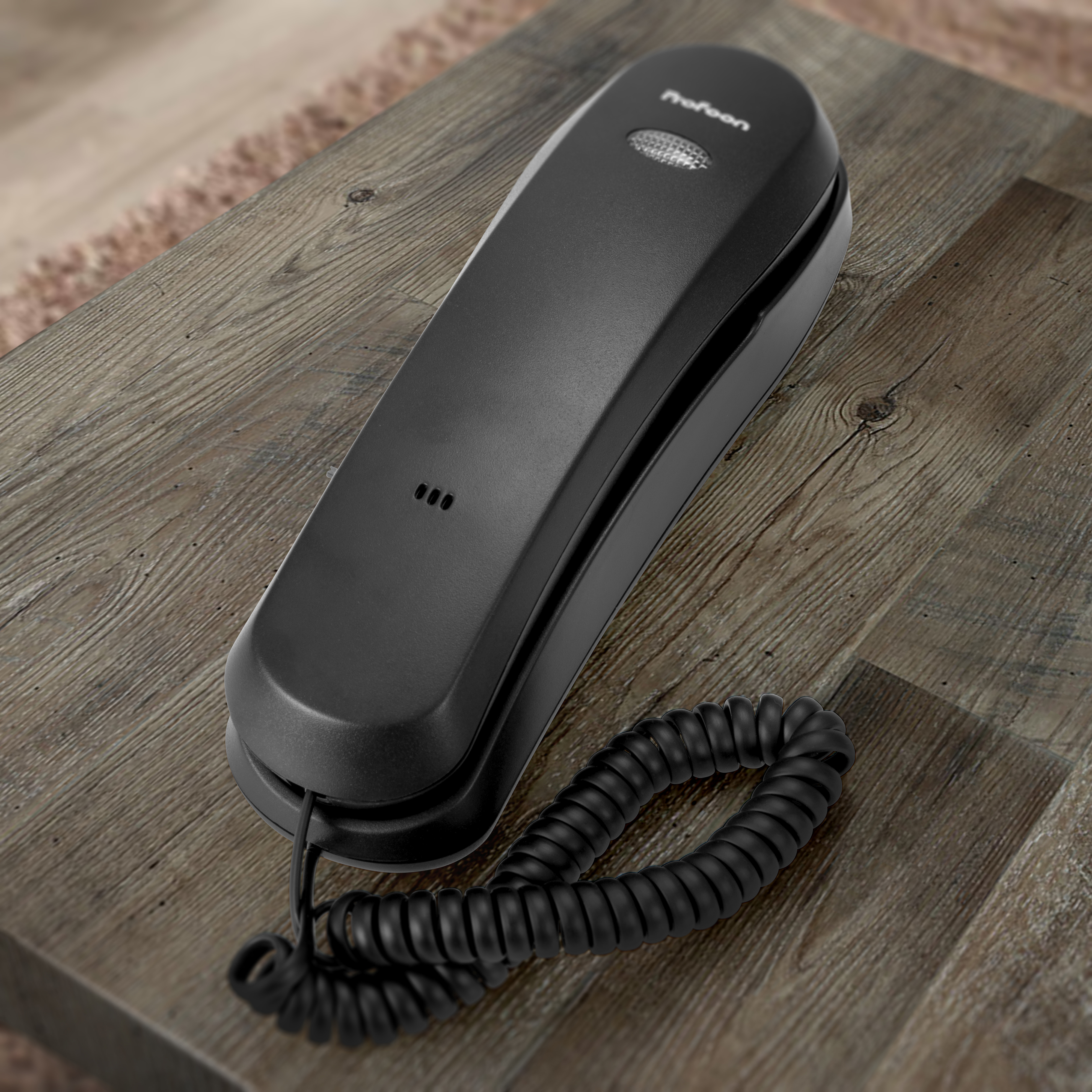 Schwarzes Festnetztelefon auf einem Holztisch, mit Spiralschnur.