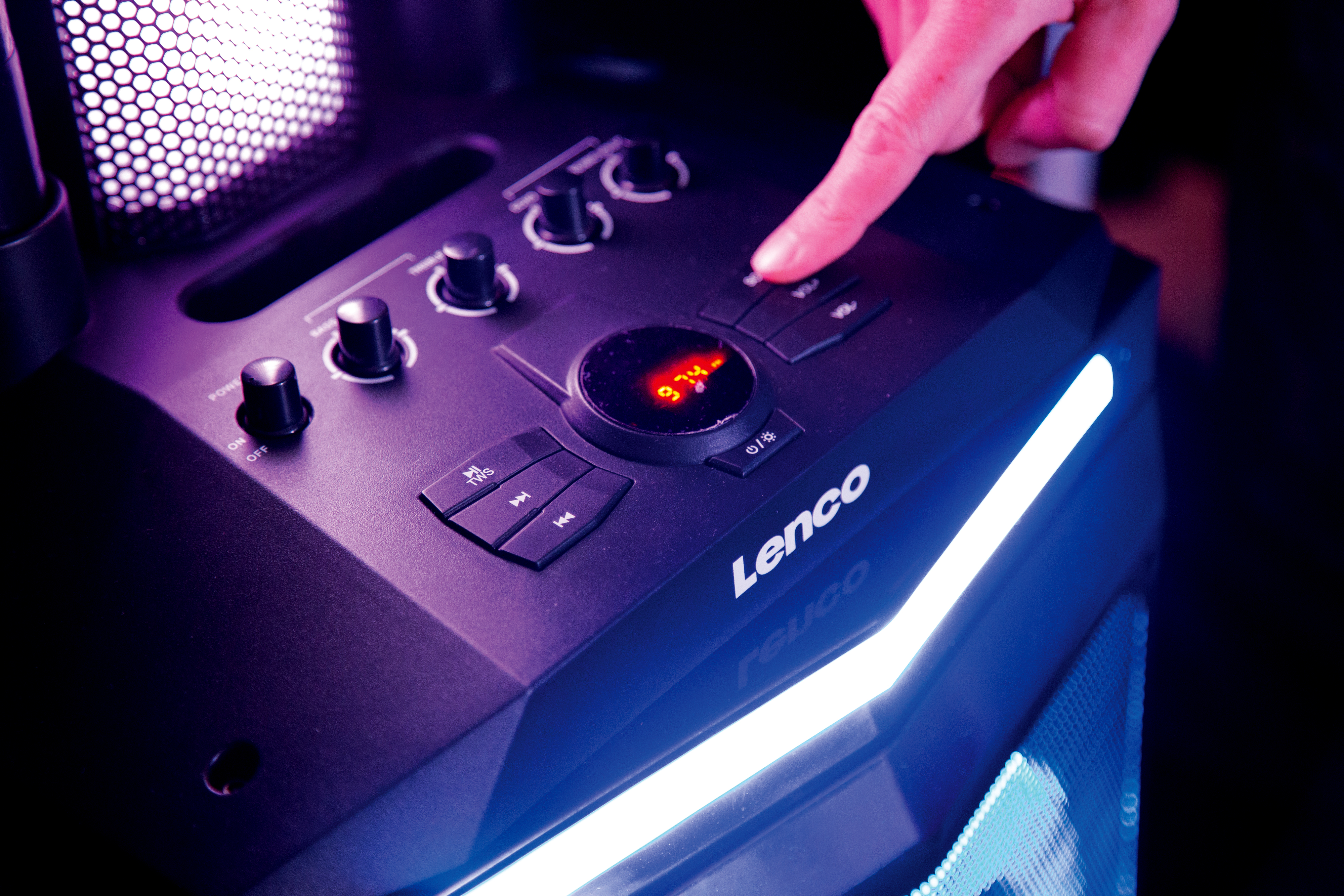 Czarny głośnik Lenco, przyciski i wyświetlacz, ręka naciskająca przycisk, niebieskie światła, ciemne tło.