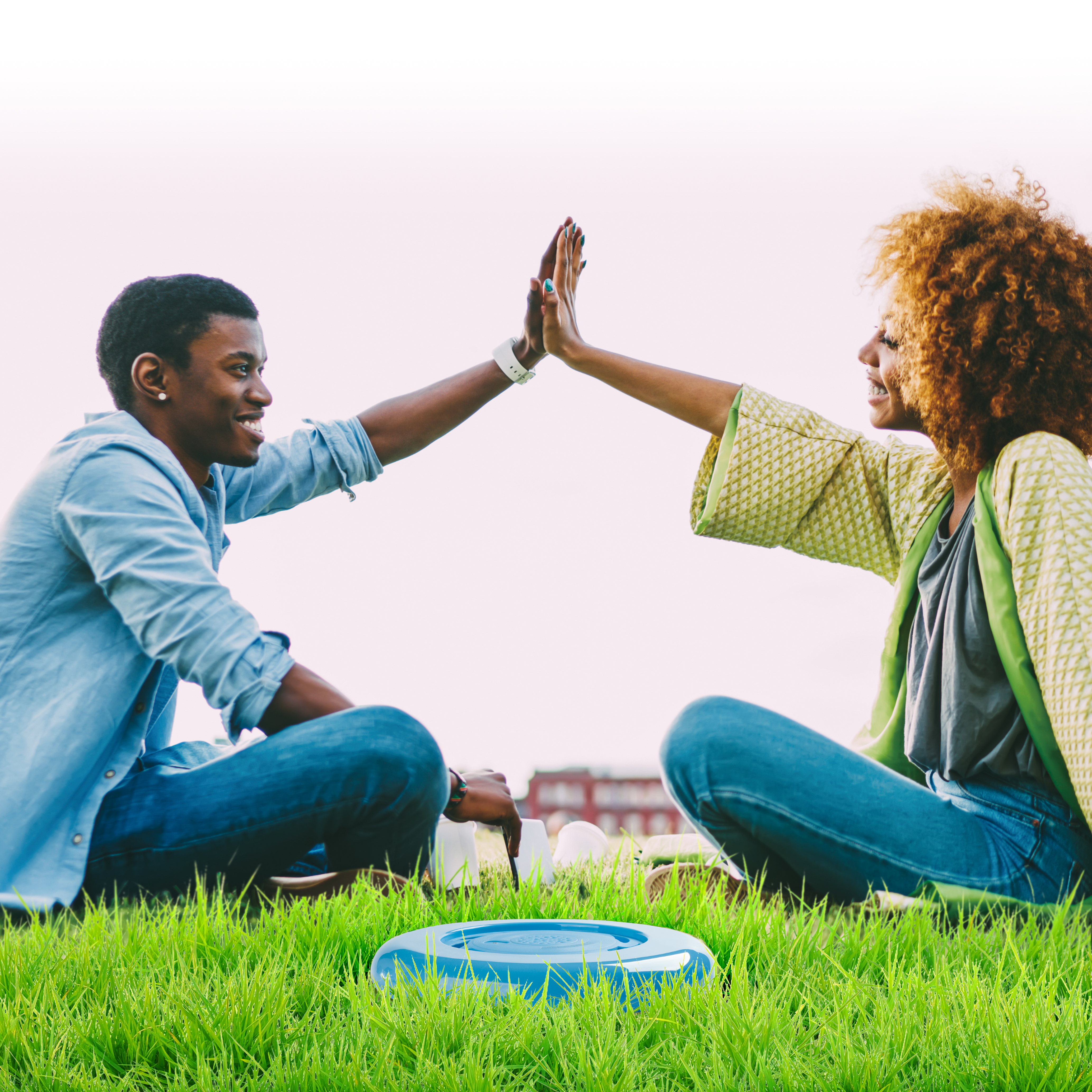 Twee mensen geven elkaar een high five op een grasveld. Een blauwe frisbee ligt op het gras.
