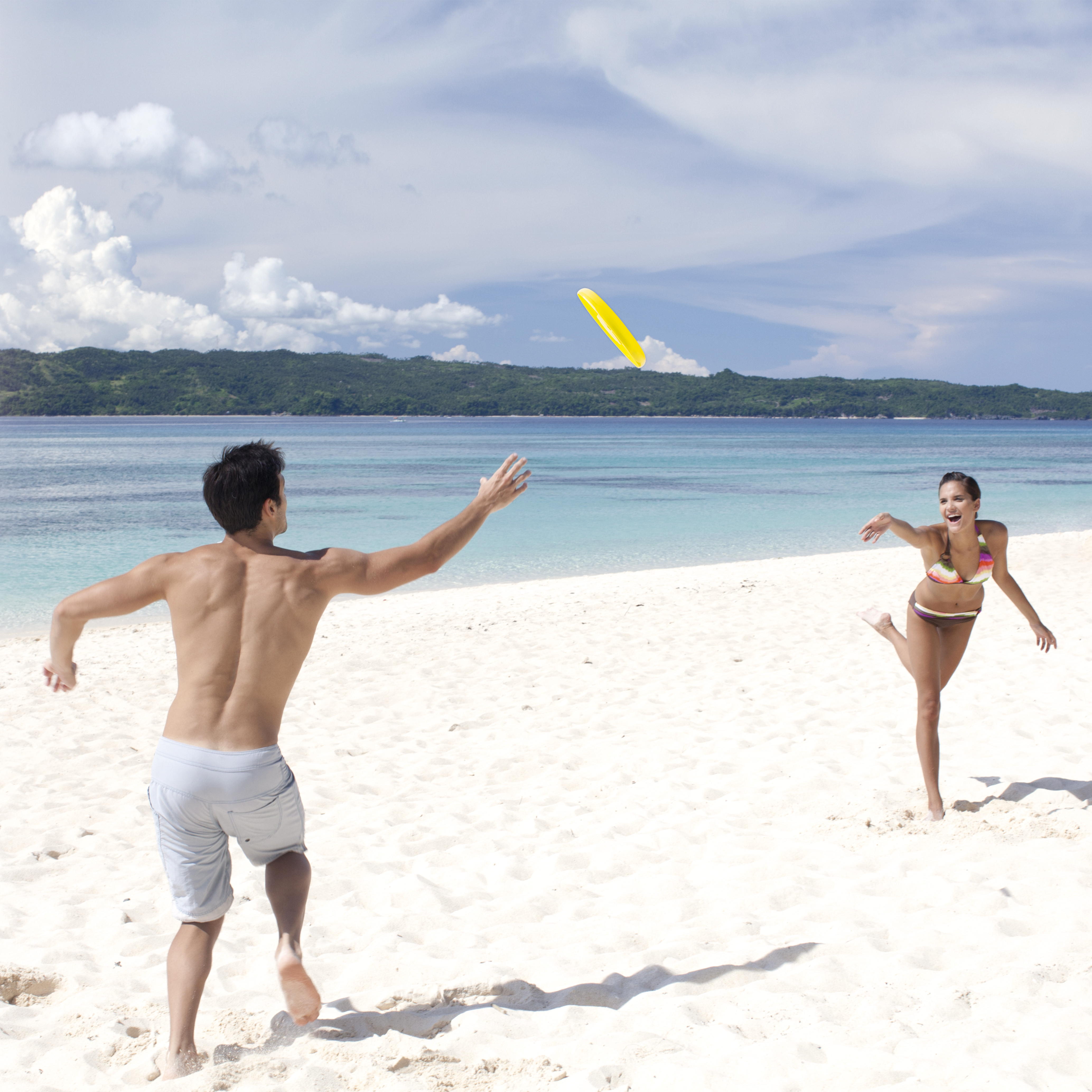 Uomo lancia frisbee giallo a donna sulla spiaggia. Mare e cielo blu.