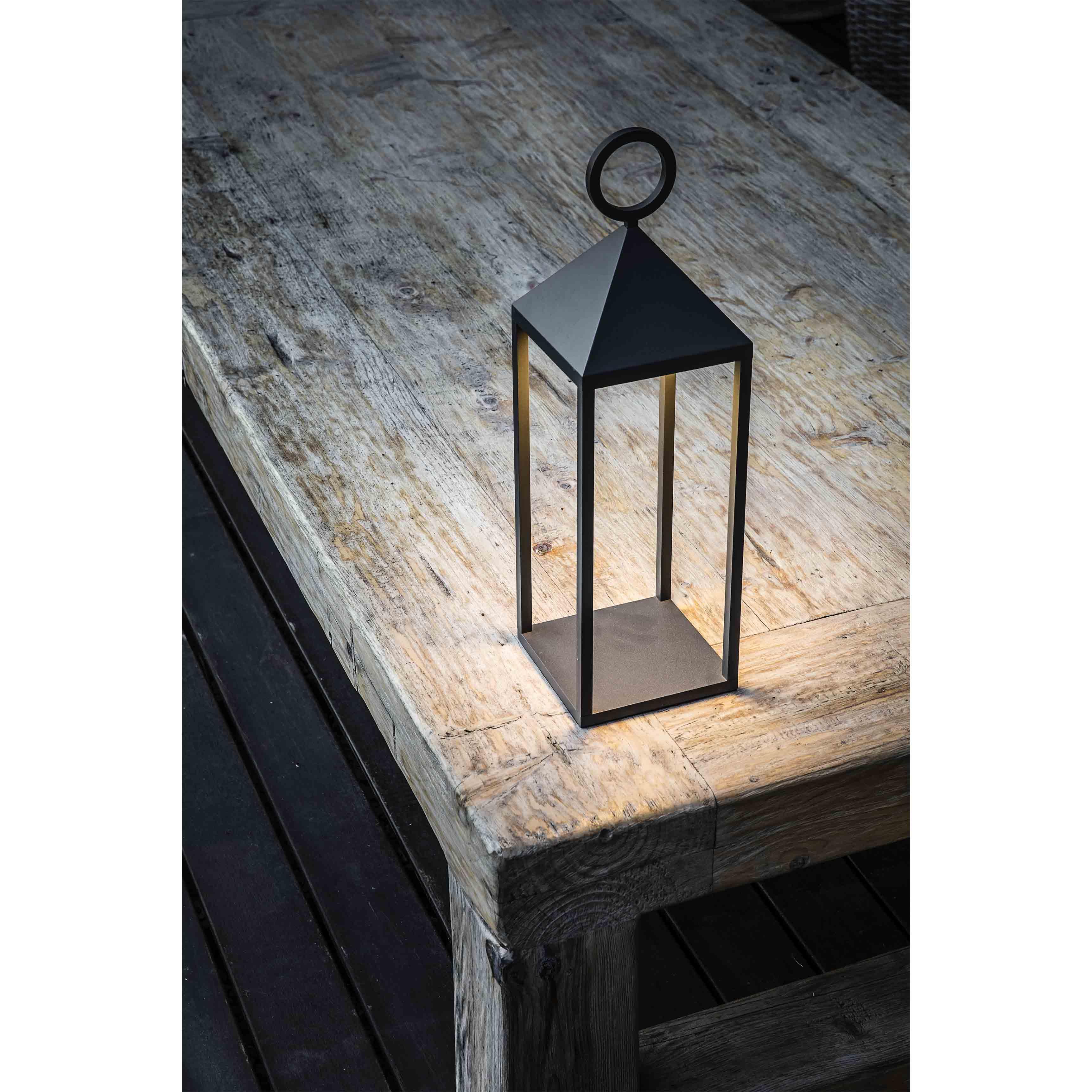 Una lanterna nera con manico è su un tavolo di legno. La lanterna è illuminata.