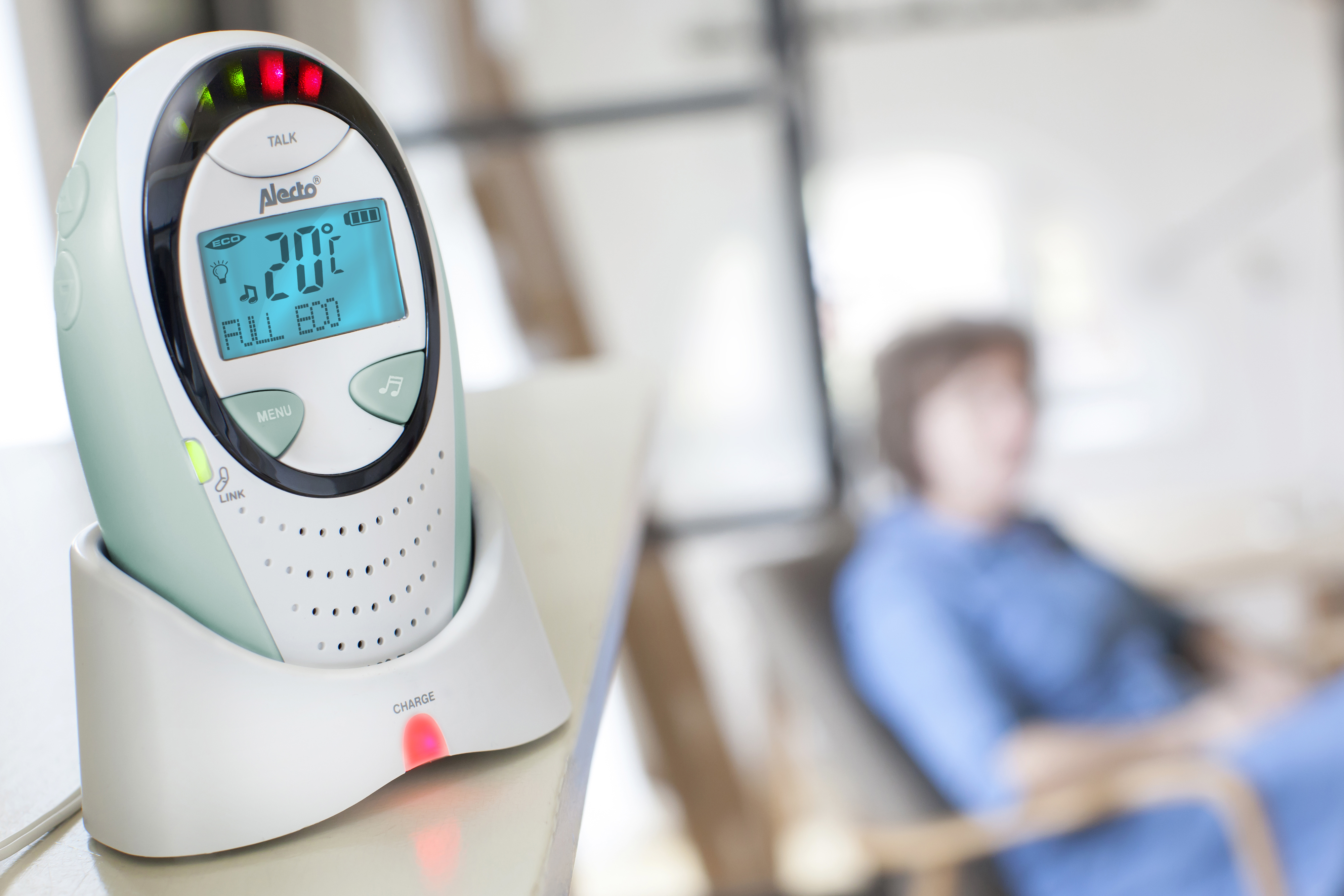 A baby monitor with a screen displaying numbers and a woman sitting in the background.