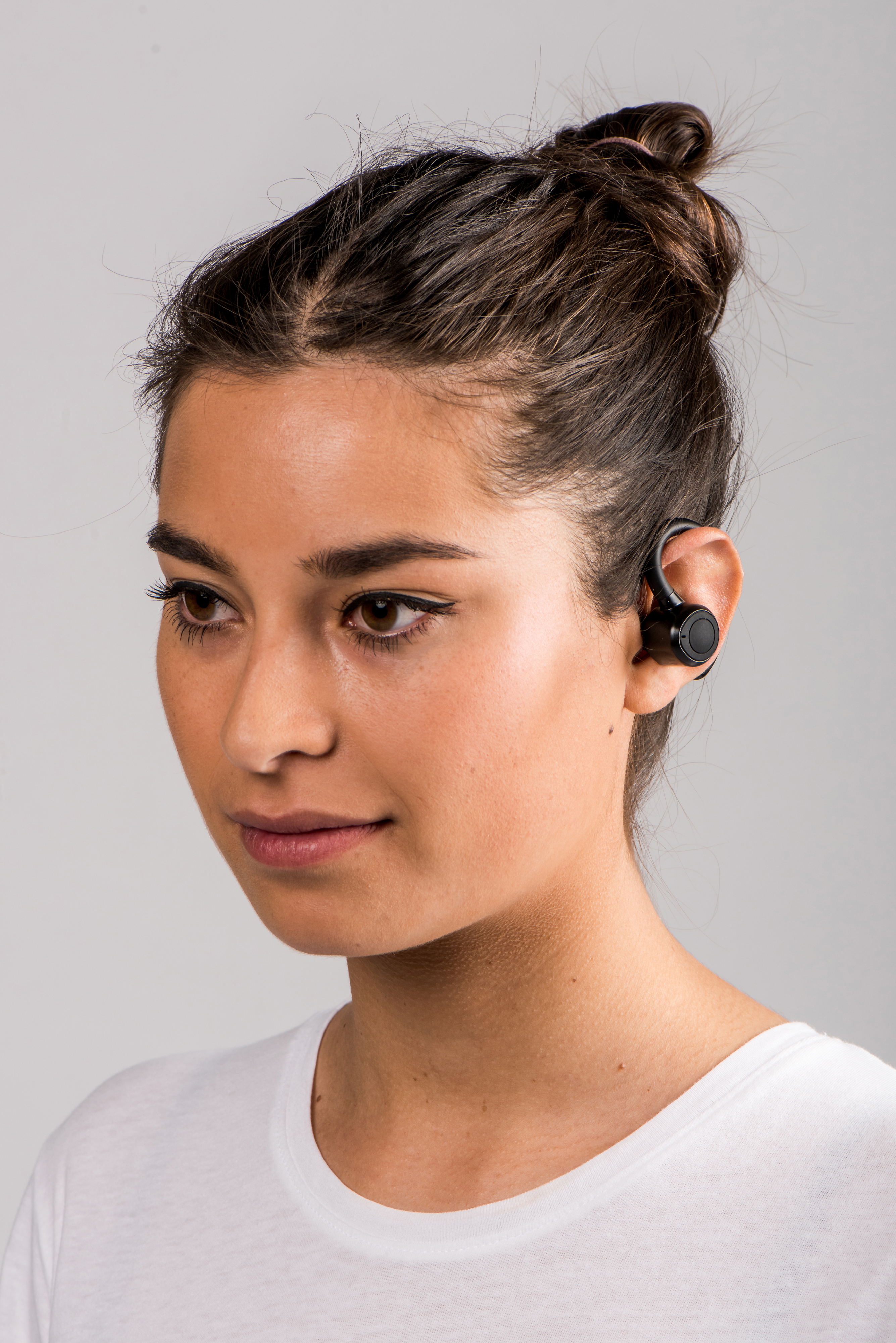 Una mujer con cabello oscuro lleva una camiseta blanca y un auricular. El auricular es negro y está alrededor de la oreja.