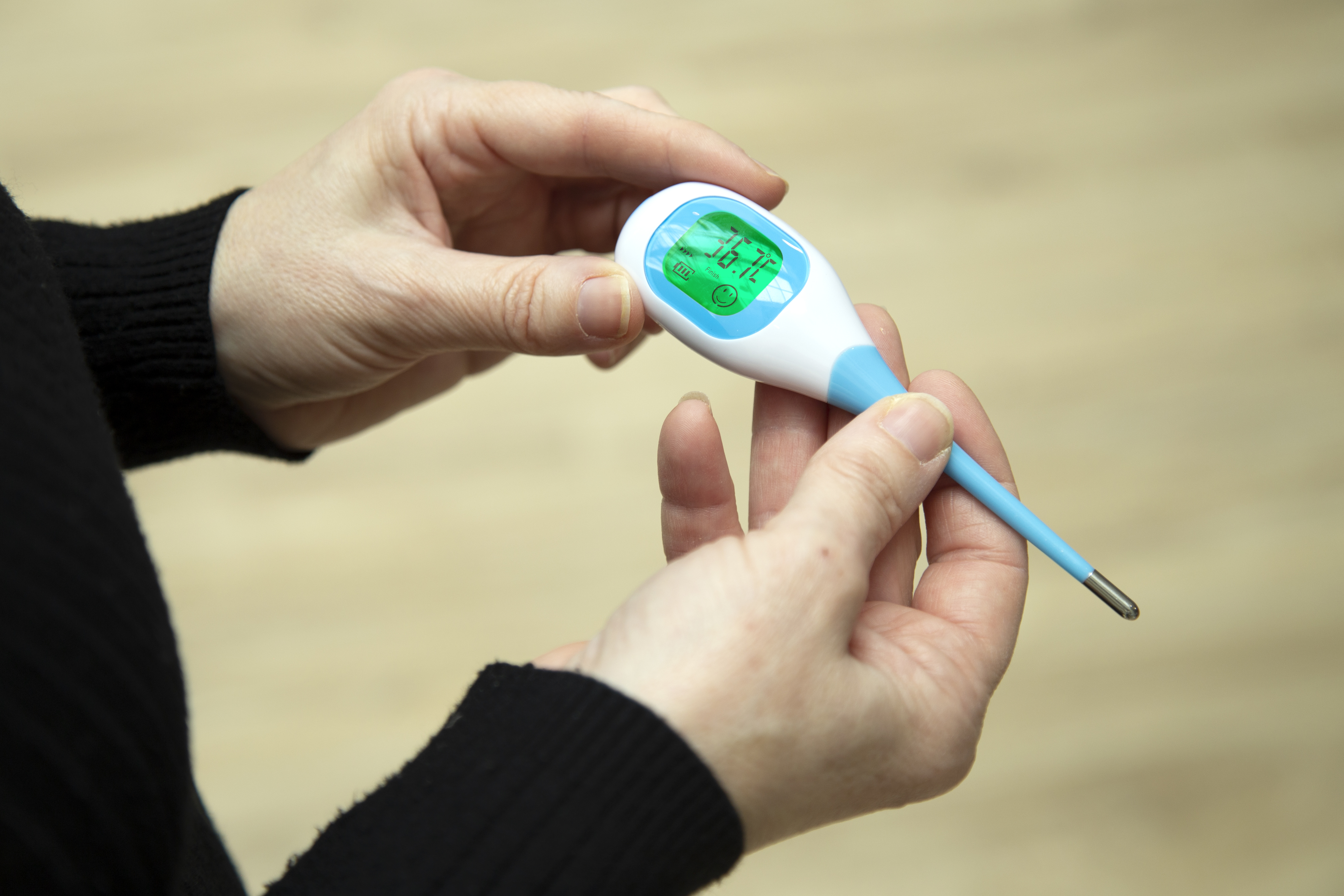Person hält ein Thermometer und zeigt 36,7 Grad Celsius auf dem Display. Verschwommener Hintergrund.