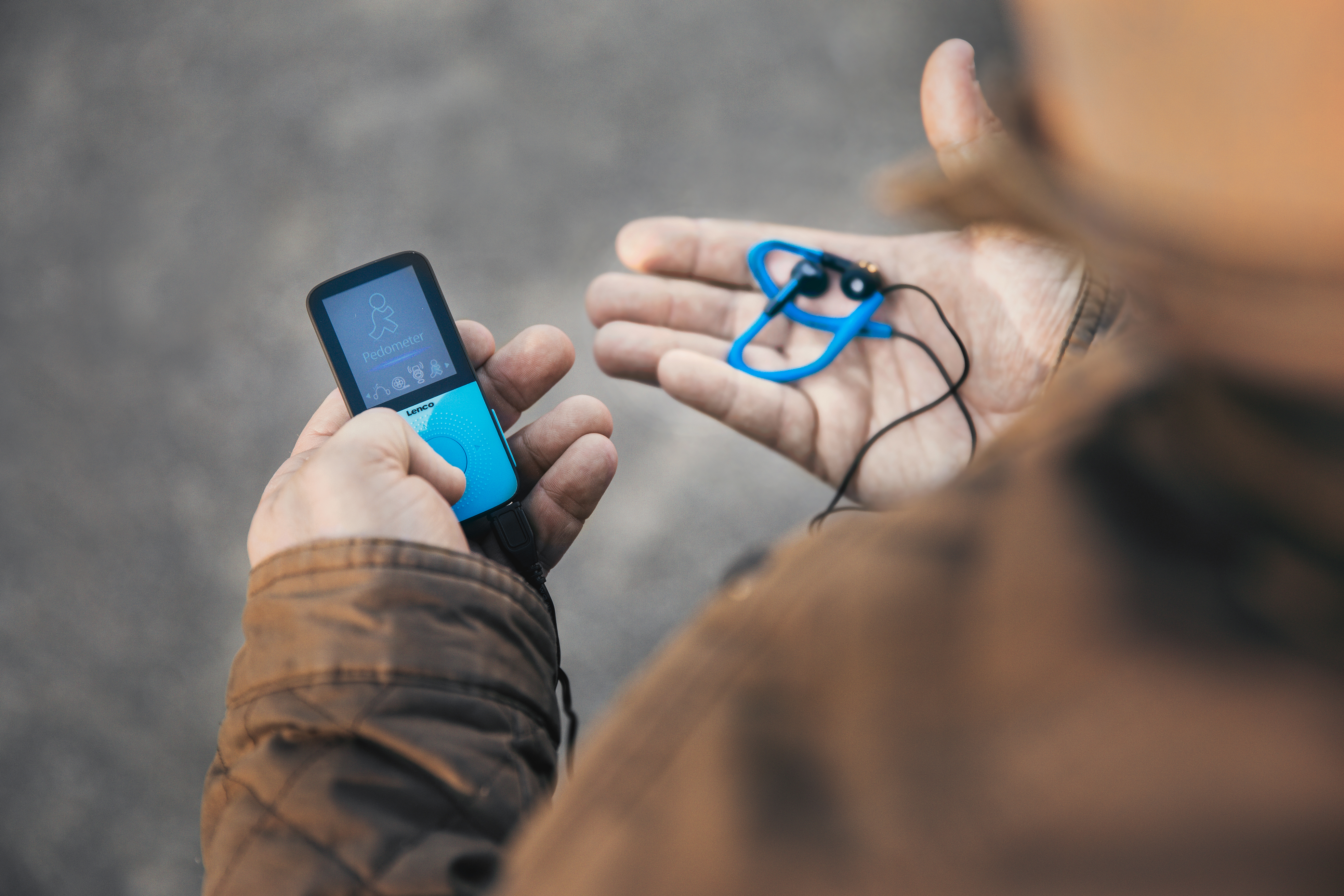 Eine Person hält einen blau-schwarzen MP3-Player und blaue Ohrhörer. Der Hintergrund ist unscharf.