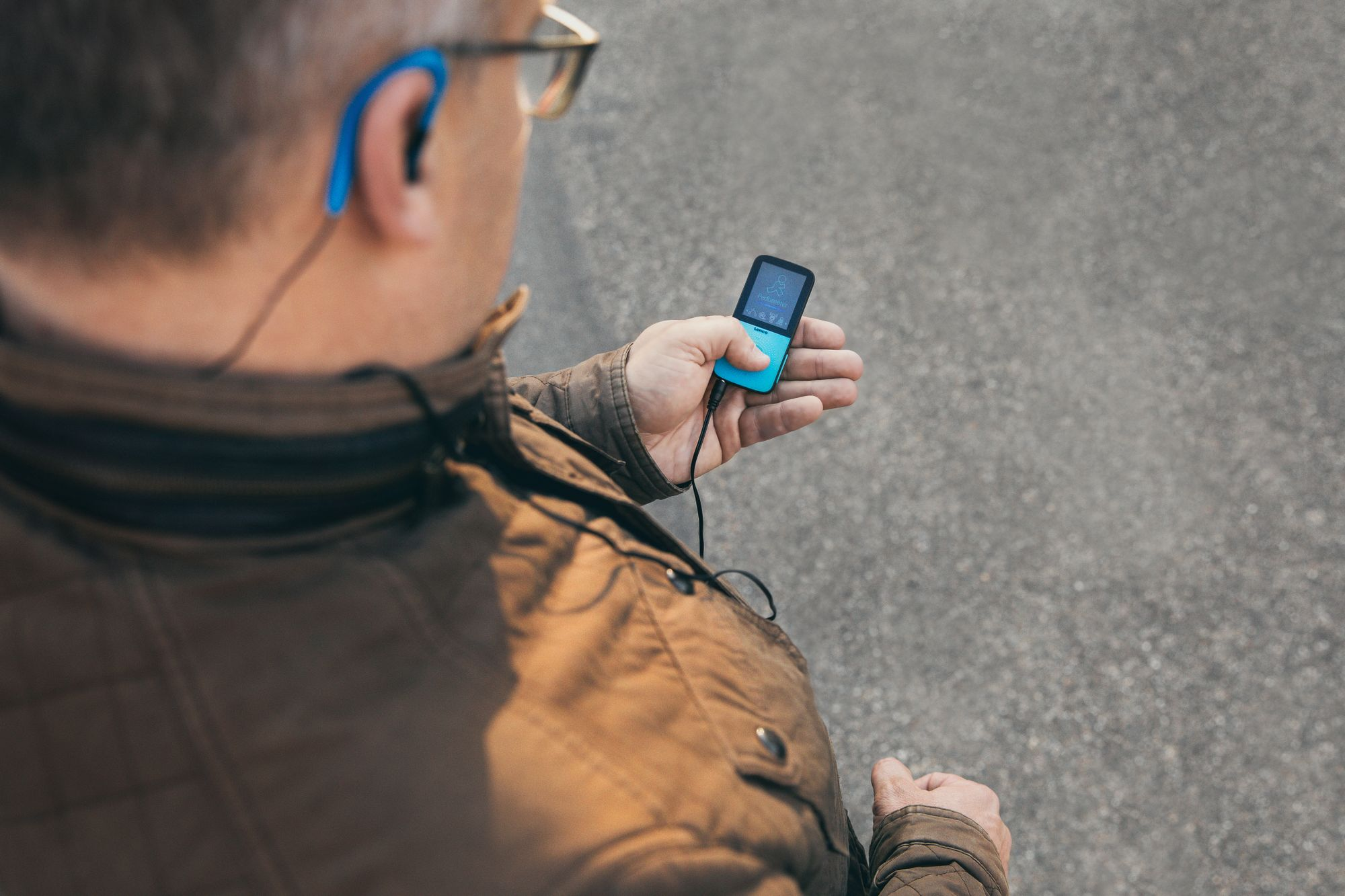 Mann, der im Freien auf einen blau-türkisfarbenen MP3-Player schaut, mit unscharfem Hintergrund.