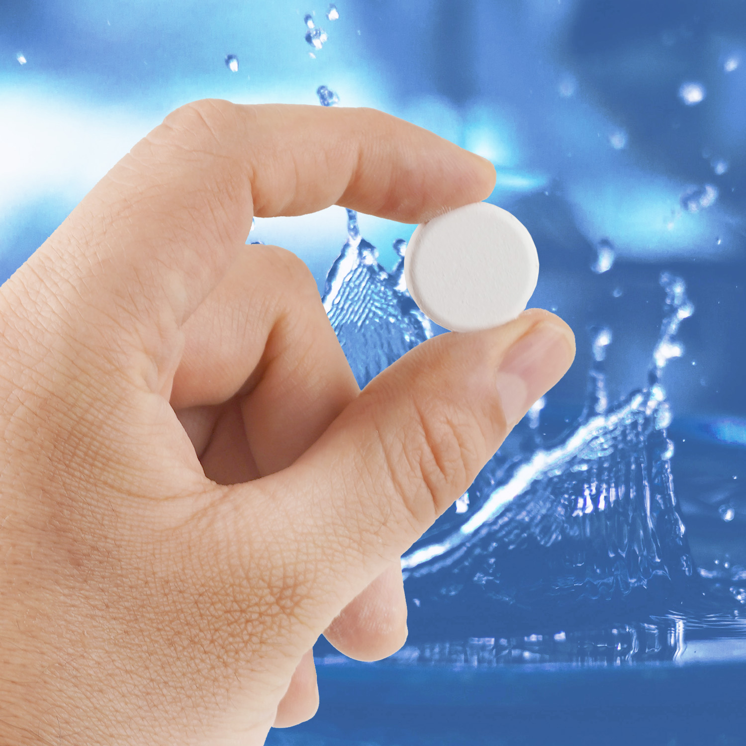 Eine Hand hält eine weiße Pille zwischen zwei Fingern. Wassertropfen und -spritzer sind im Hintergrund.