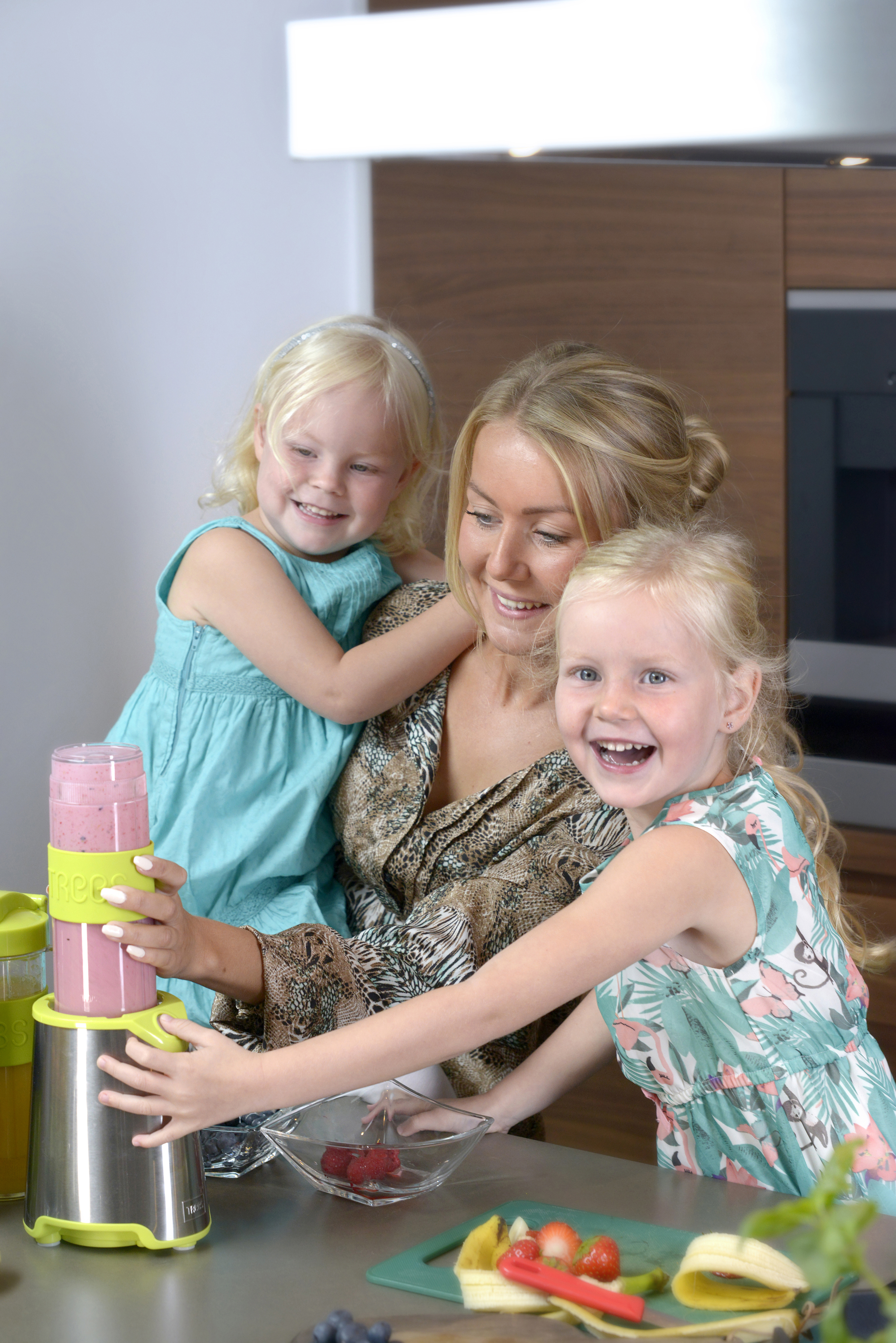 Donna e due bambini con un frullatore che prepara una bevanda. Ambiente cucina.