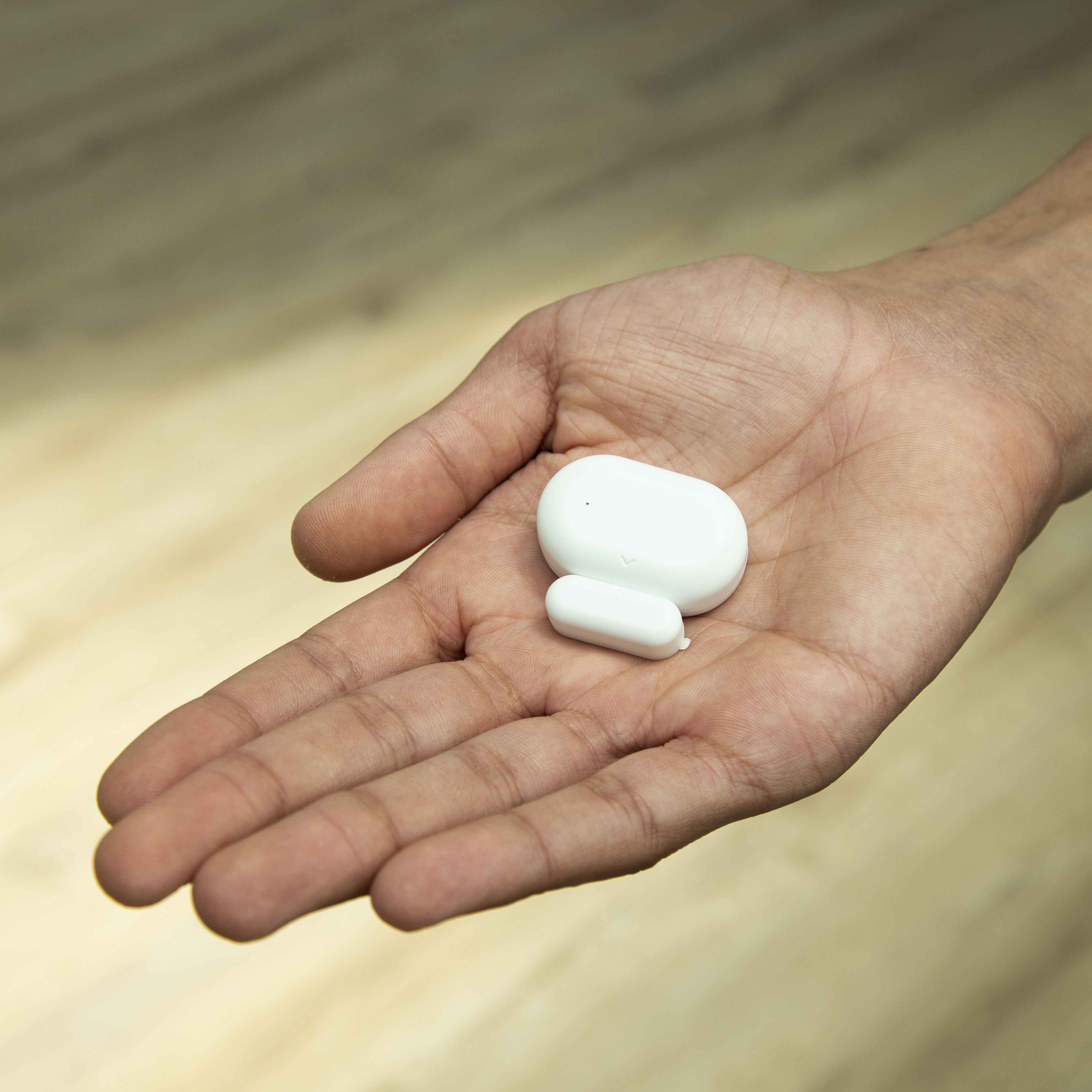 Eine Hand hält ein weißes, oval geformtes Gerät und ein kleineres weißes Rechteck.
