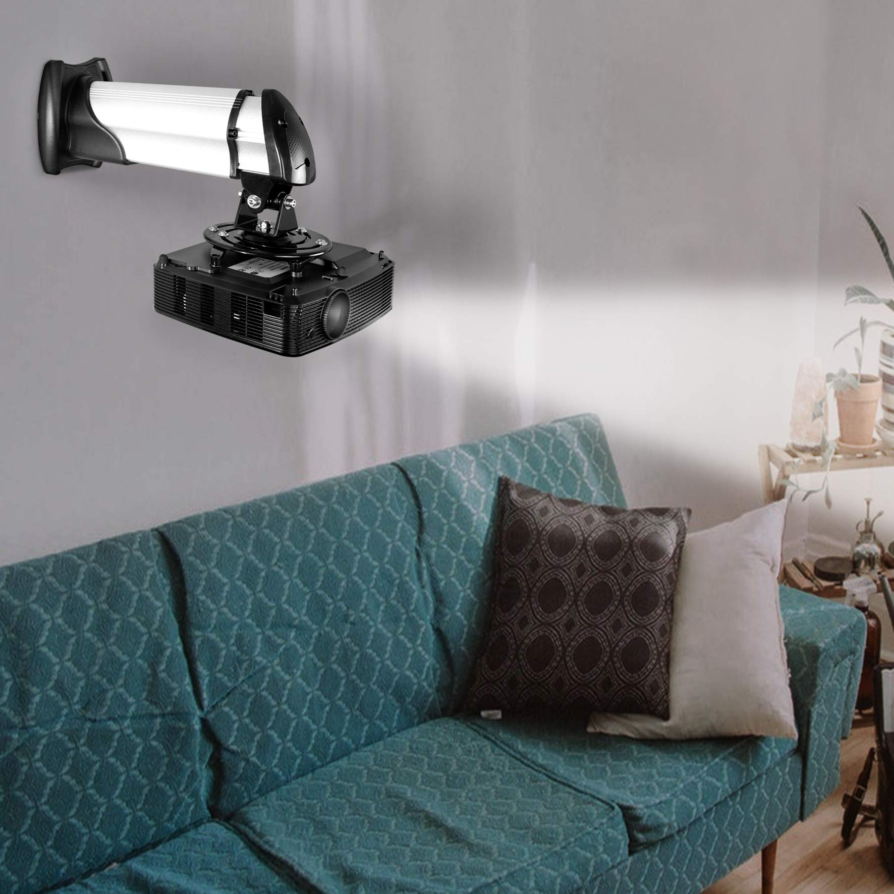 Un proyector negro está montado en una pared blanca. Un sofá y una planta están en primer plano.