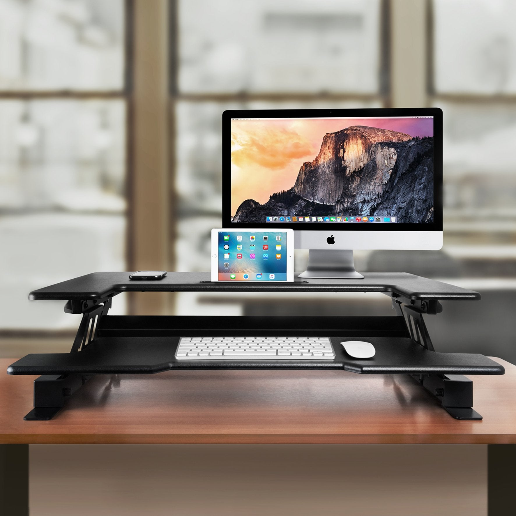 Schwarzer Schreibtisch mit Computer, Tablet, Tastatur und Maus, braune Holzoberfläche.