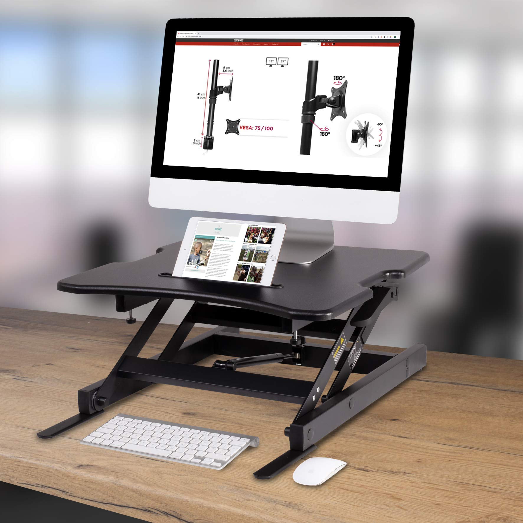Escritorio negro con monitor y tableta, teclado y ratón. El escritorio está sobre una mesa de madera con diagramas.