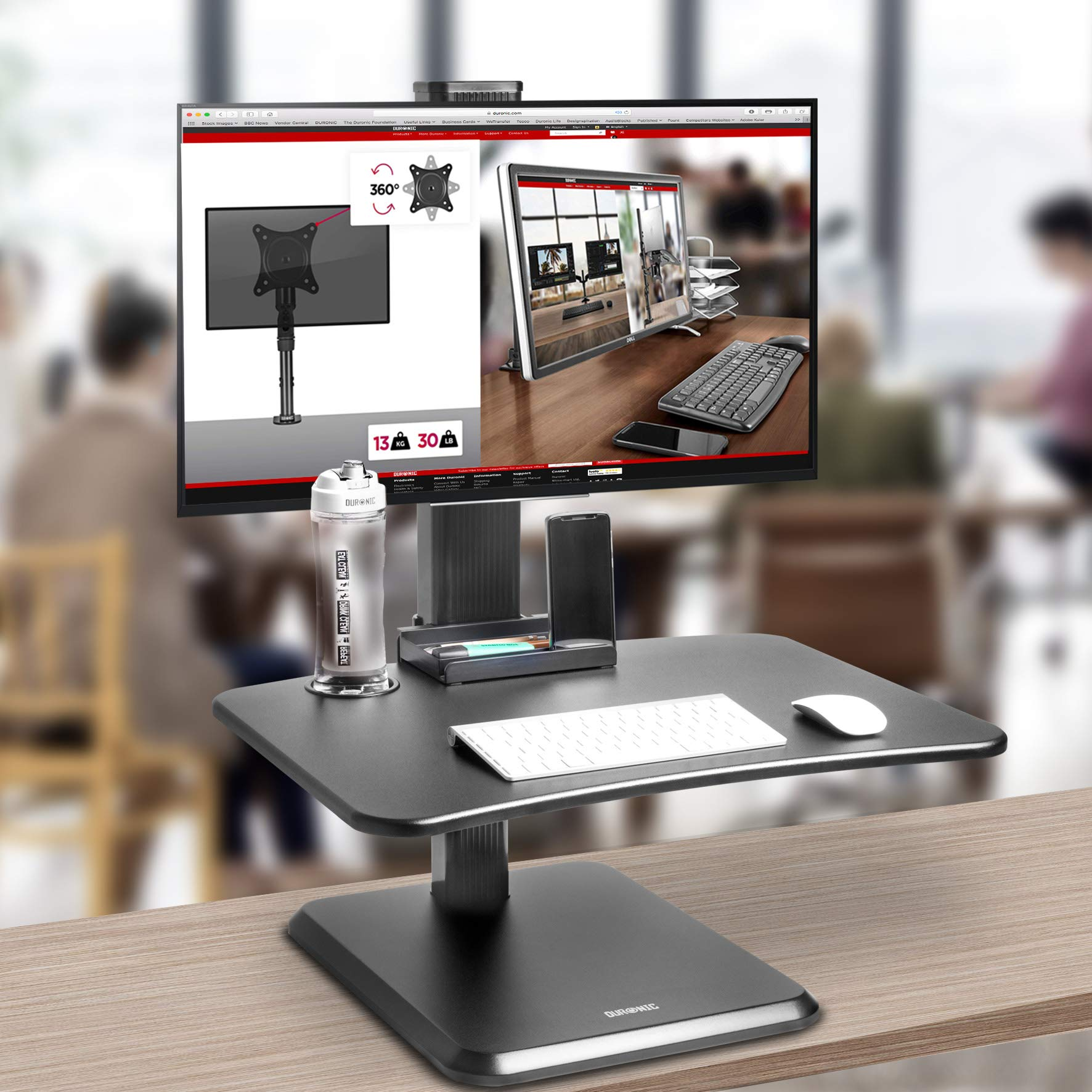 Una configuración de escritorio con monitor, soporte, teclado, ratón y botella de agua. El fondo está borroso.