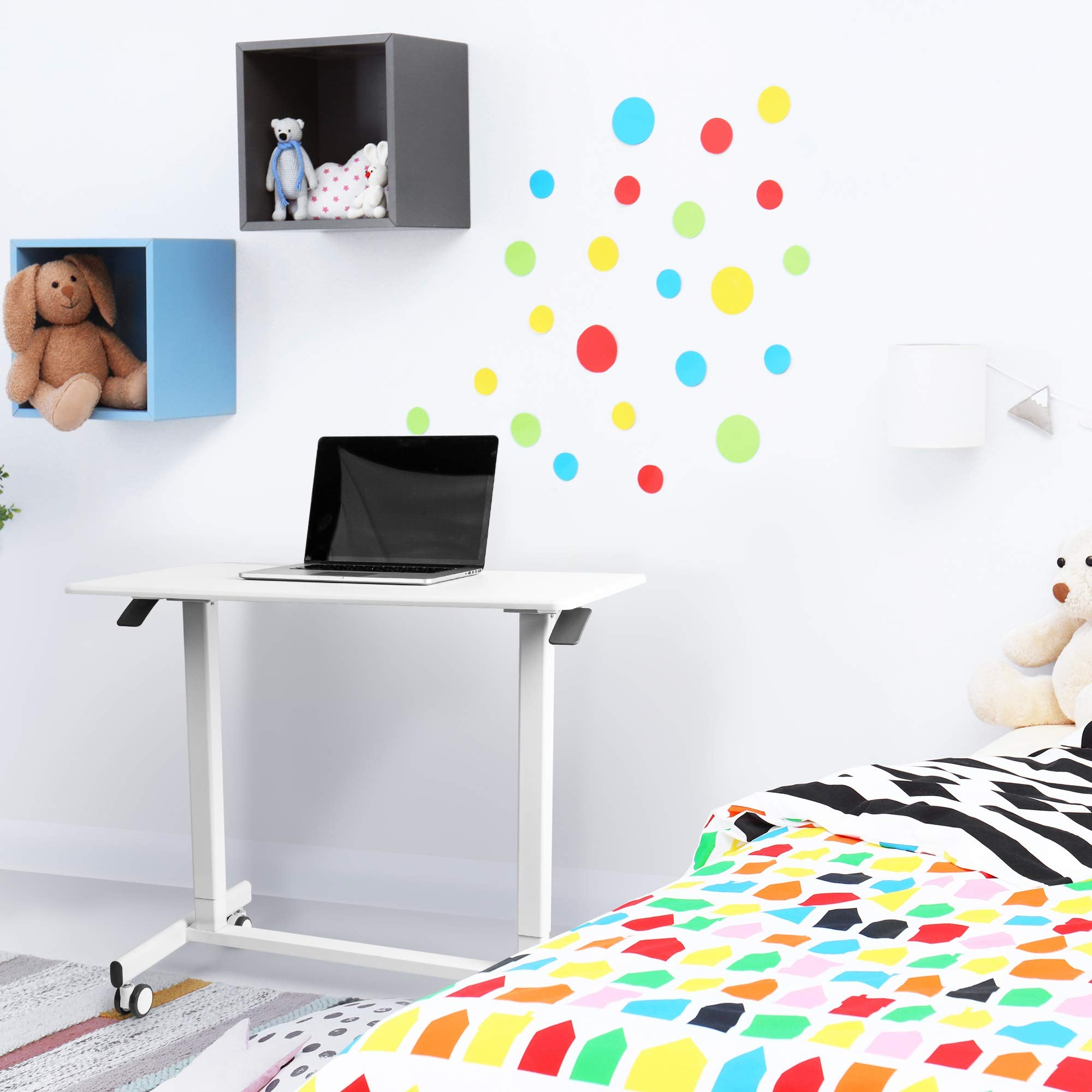 Un escritorio con un portátil, una cama y calcomanías de pared coloridas en un dormitorio infantil.