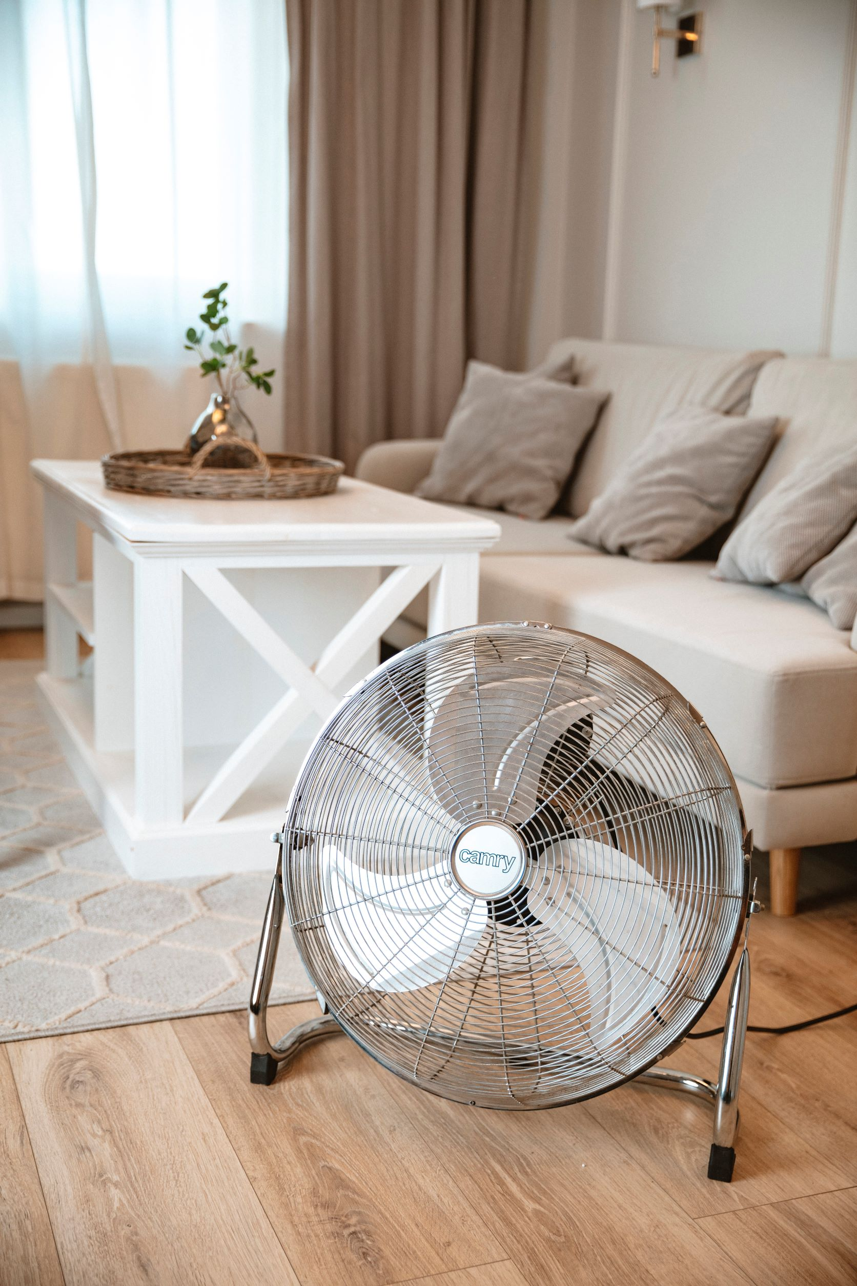Ein silberner Ventilator auf einem Ständer in einem Wohnzimmer mit Sofa und Couchtisch.