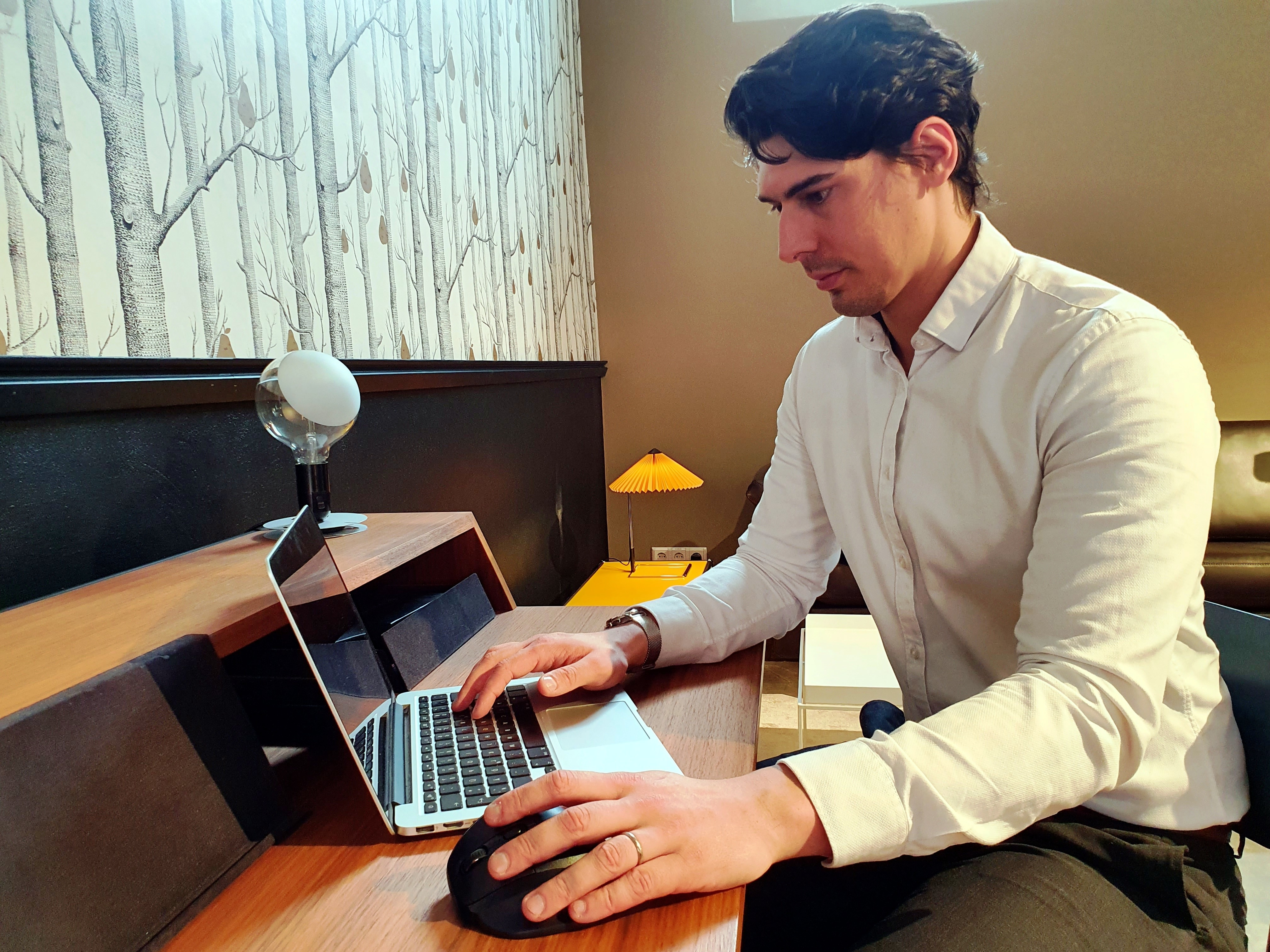 Ein Mann arbeitet an einem Laptop an einem Holzschreibtisch. Auf dem Schreibtisch steht eine Lampe.
