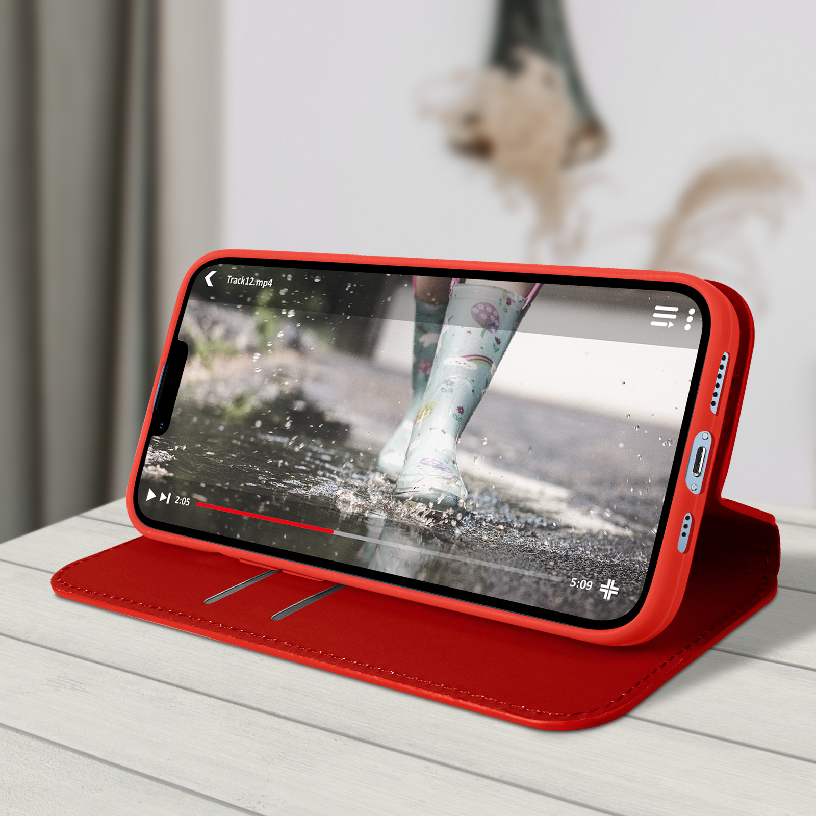 Un smartphone dans un étui rouge affiche une vidéo de pieds marchant dans l'eau. L'étui est sur une table en bois.