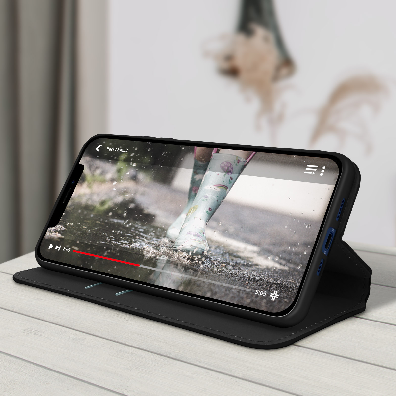 Custodia nera per telefono con un telefono che mostra un video. Una persona indossa stivali da pioggia.