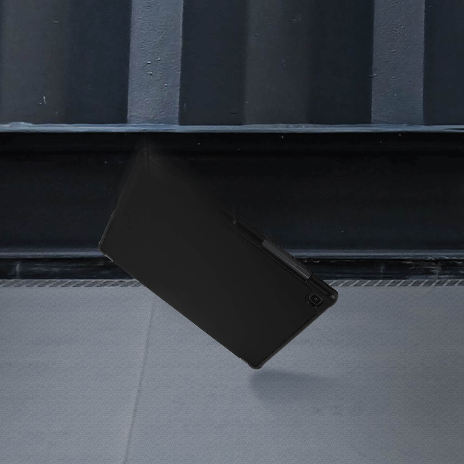 Una custodia nera per tablet che cade, ripresa su sfondo scuro con superficie metallica.