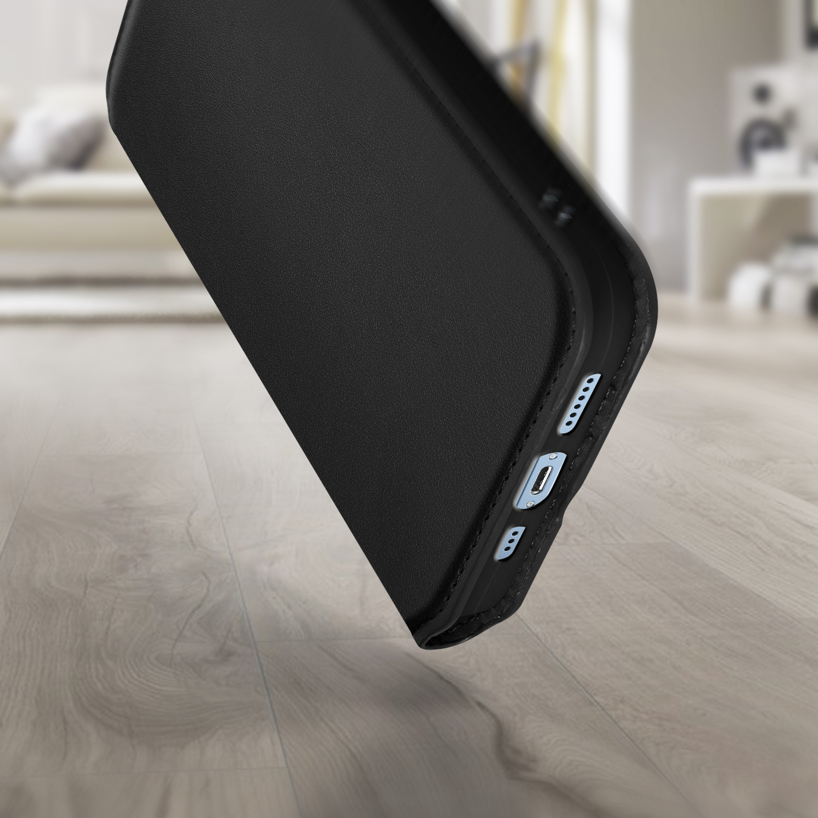 Custodia nera per telefono su pavimento in legno, inclinata. Sfondo sfocato.
