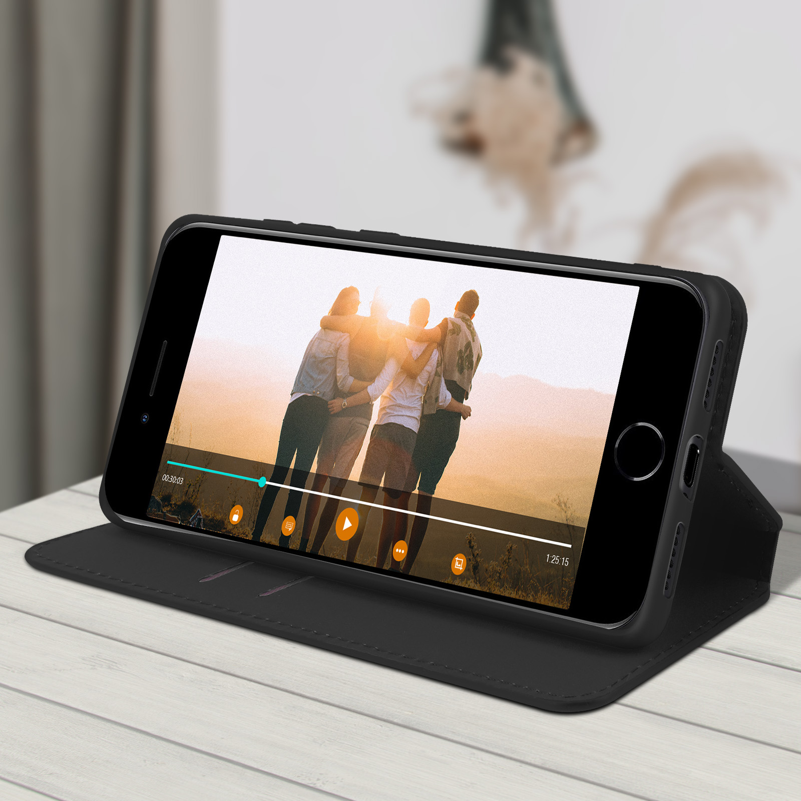 Téléphone dans un étui noir affichant une vidéo de personnes. Table et fenêtre en arrière-plan.