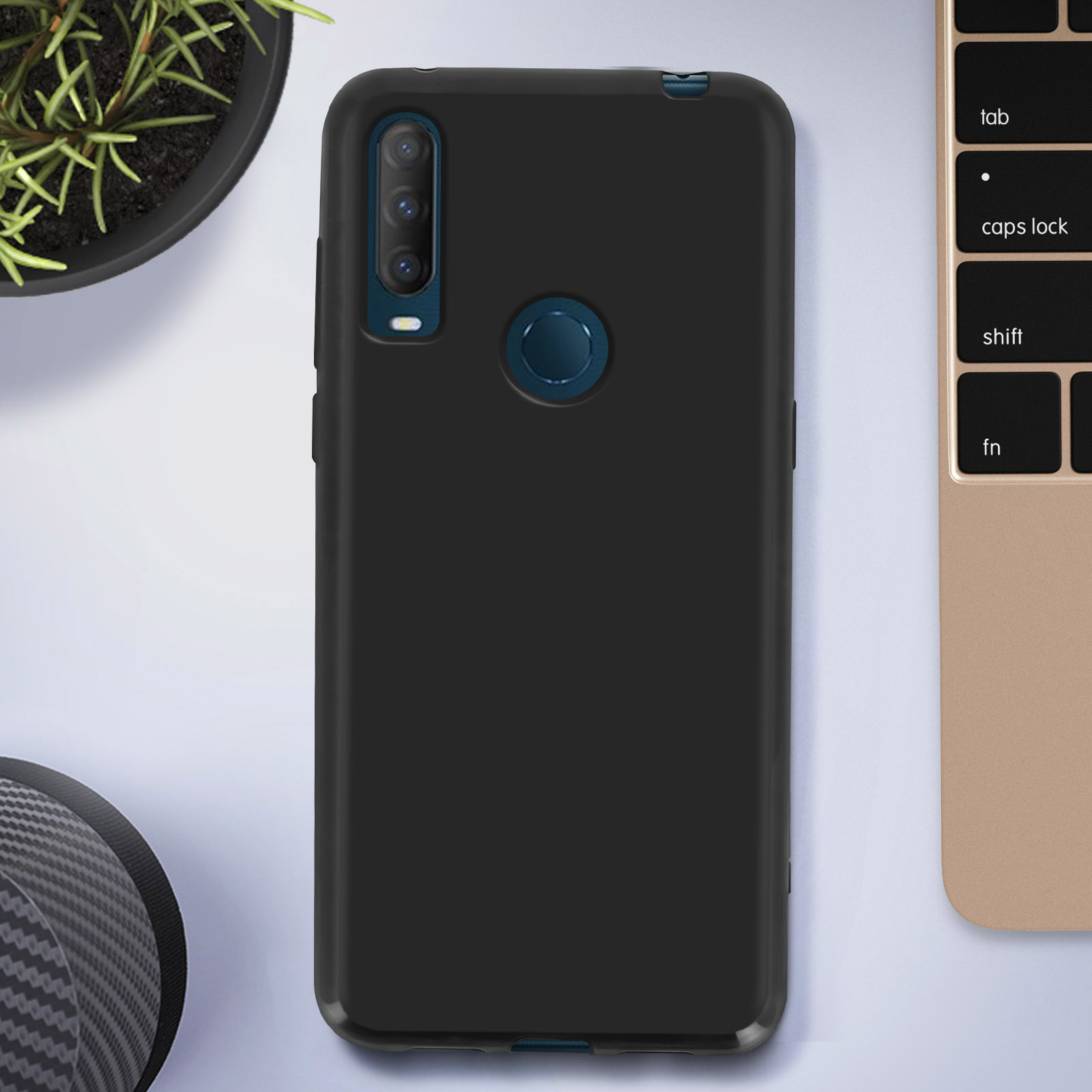 Coque de téléphone noire sur une surface blanche, à côté d'une plante et d'un clavier d'ordinateur portable.