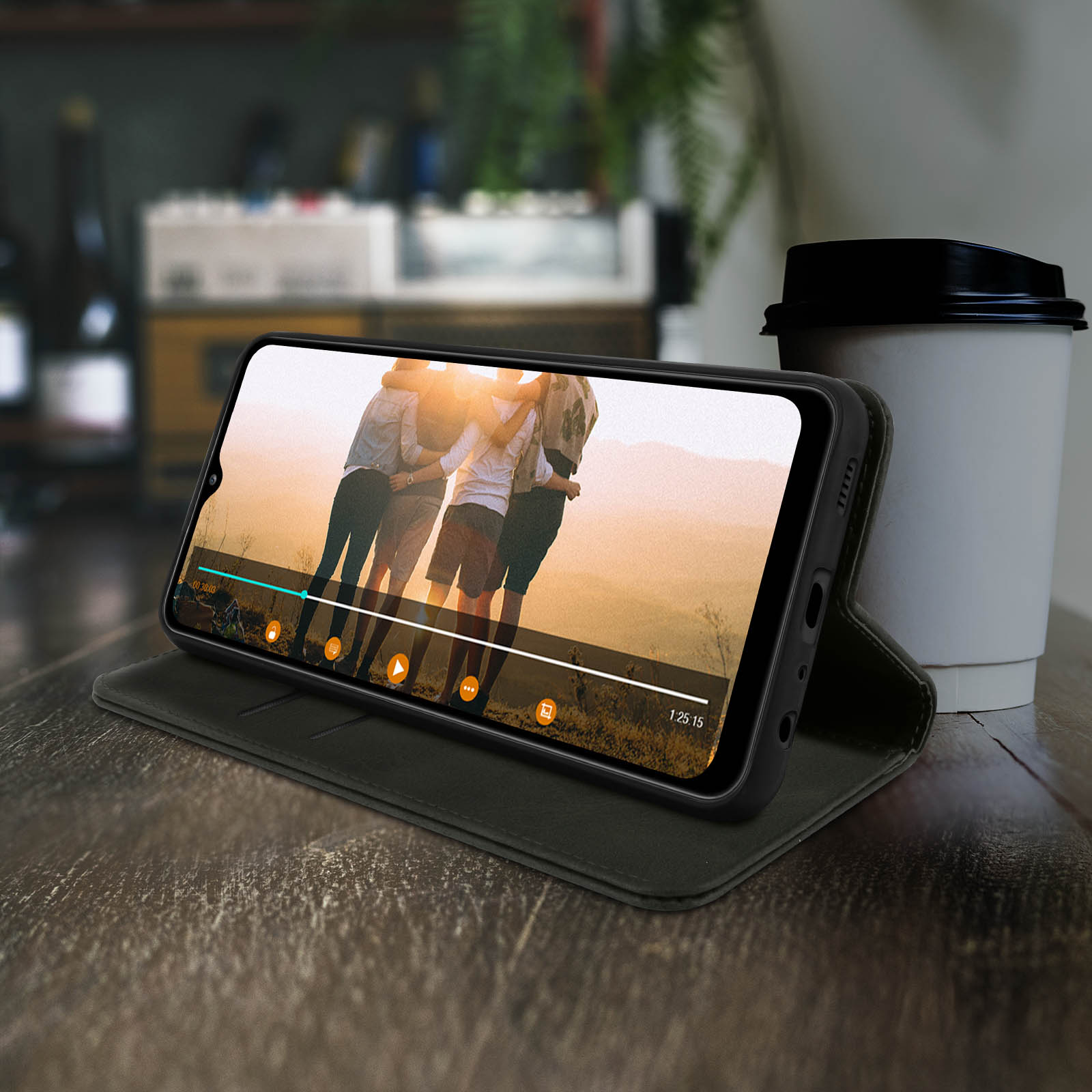 Telefono in custodia mostra video, con tazza di caffè su tavolo di legno.