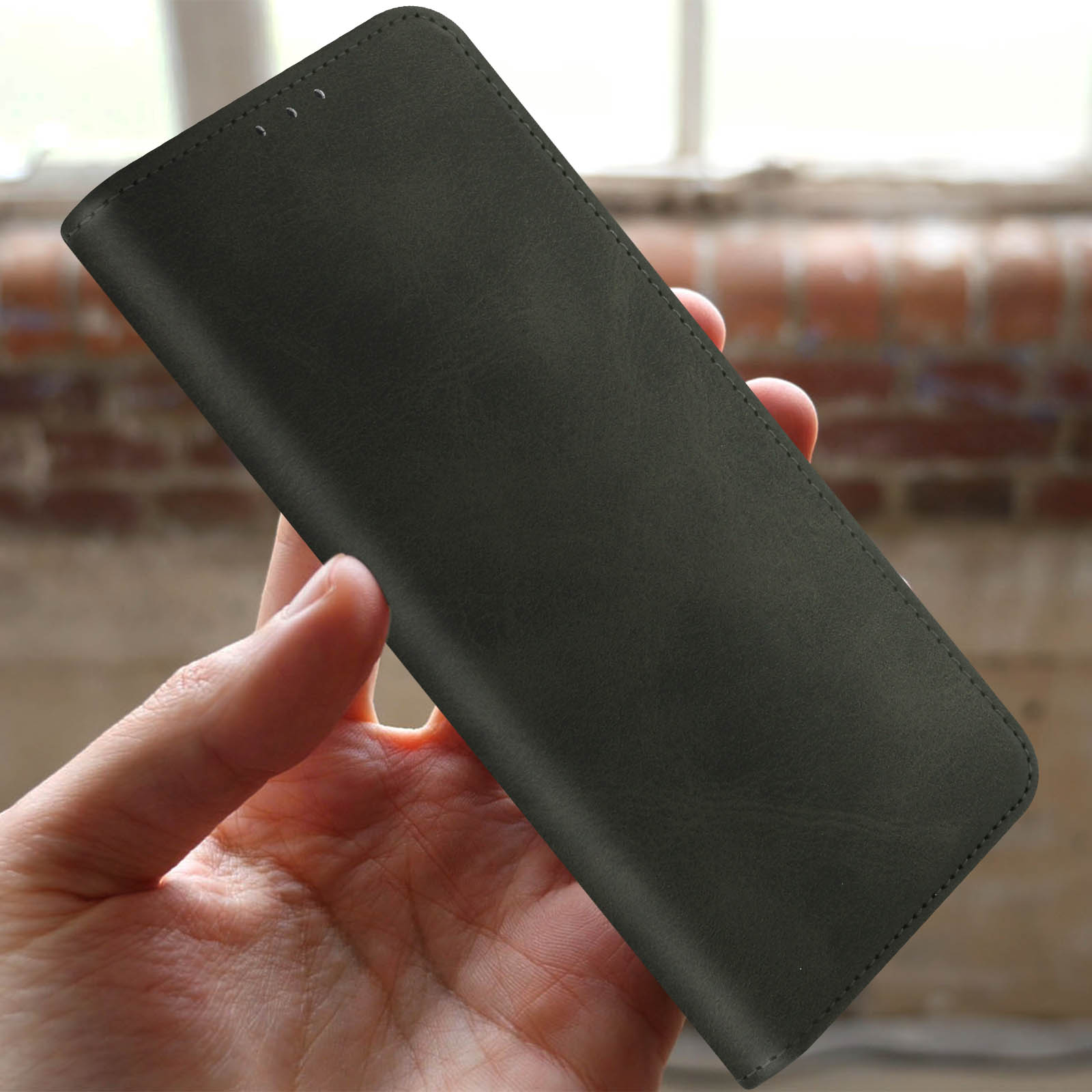 Mano che tiene una custodia nera per telefono, all'interno di una stanza con luce naturale.