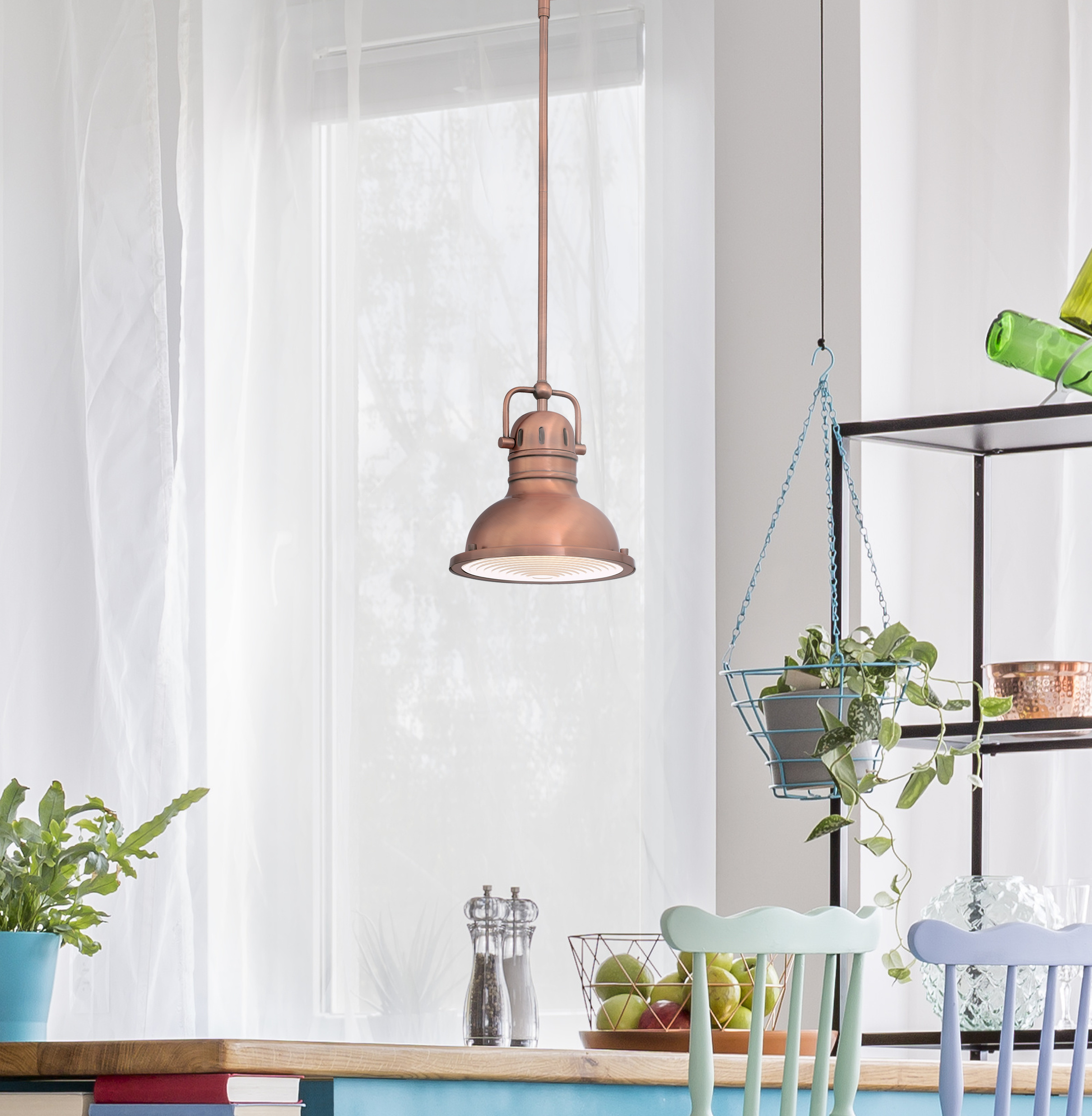 Eine kupferfarbene Pendelleuchte hängt über einem Tisch mit Stühlen. Der Hintergrund umfasst ein Fenster mit Vorhängen und Pflanzen.
