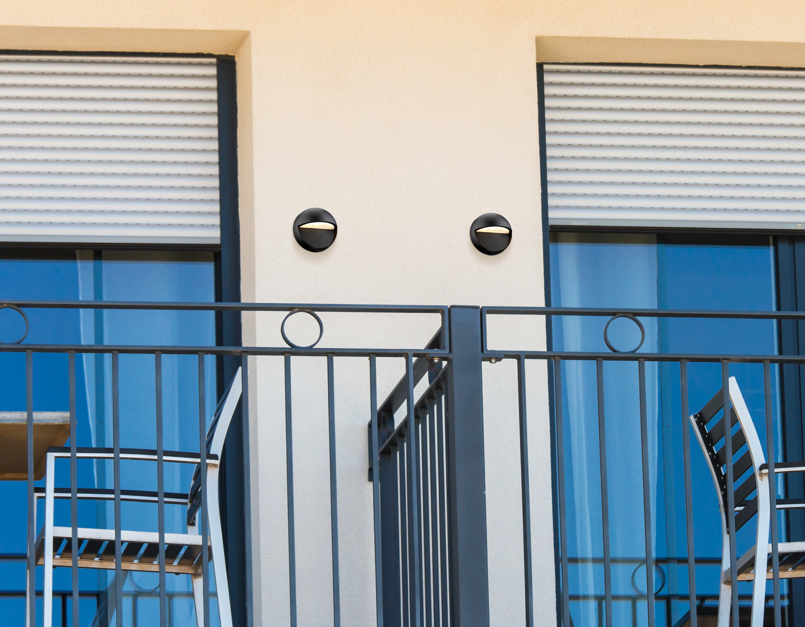 Balkon mit zwei Wandleuchten, einem Geländer und geschlossenen Jalousien.