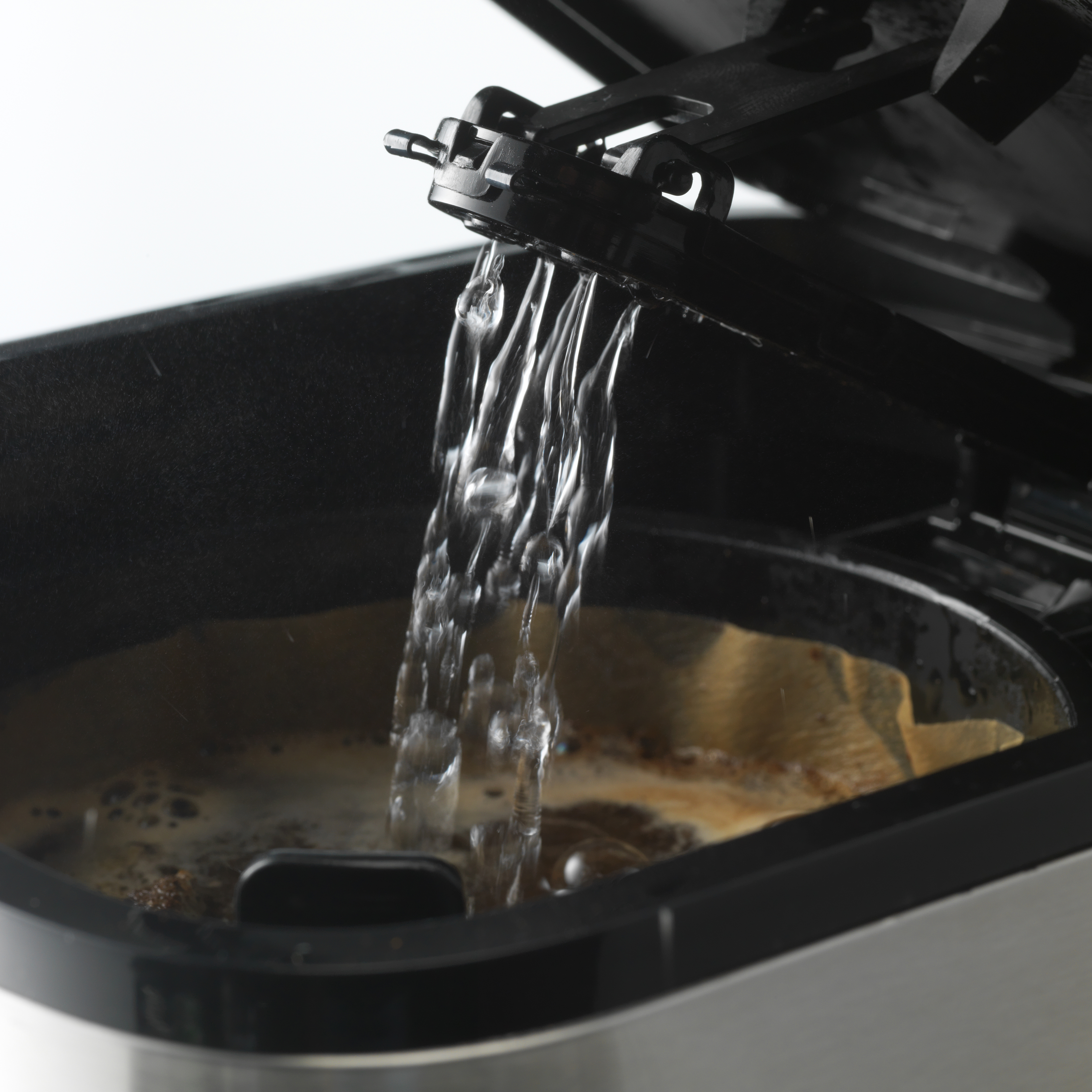 Wasser gießt in eine Kaffeemaschine. Der Filter und das Kaffeepulver sind sichtbar. Die Maschine ist offen.