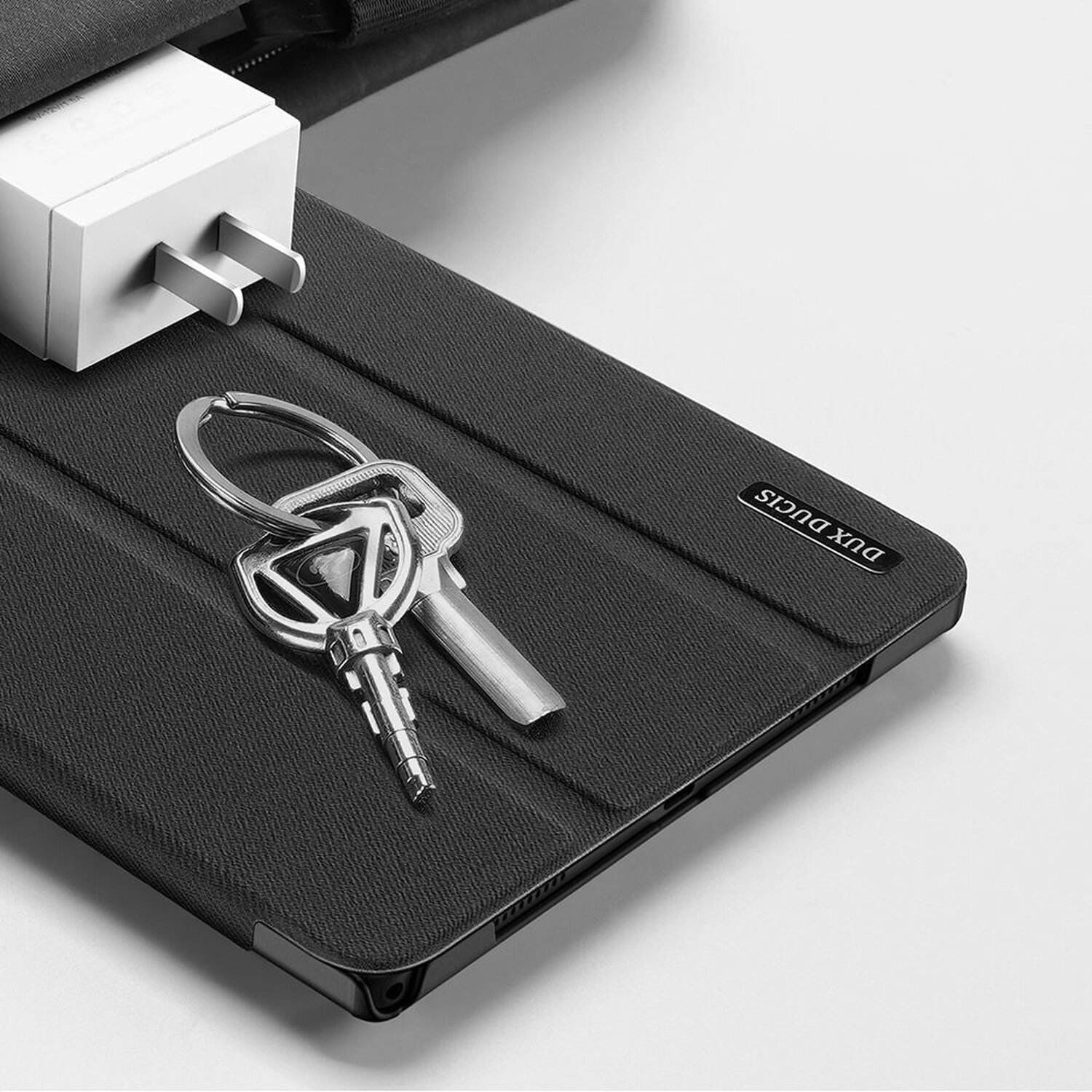 Schlüssel und Ladegerät auf schwarzer Tablet-Hülle. Die Hülle hat 'Dux Ducis'.