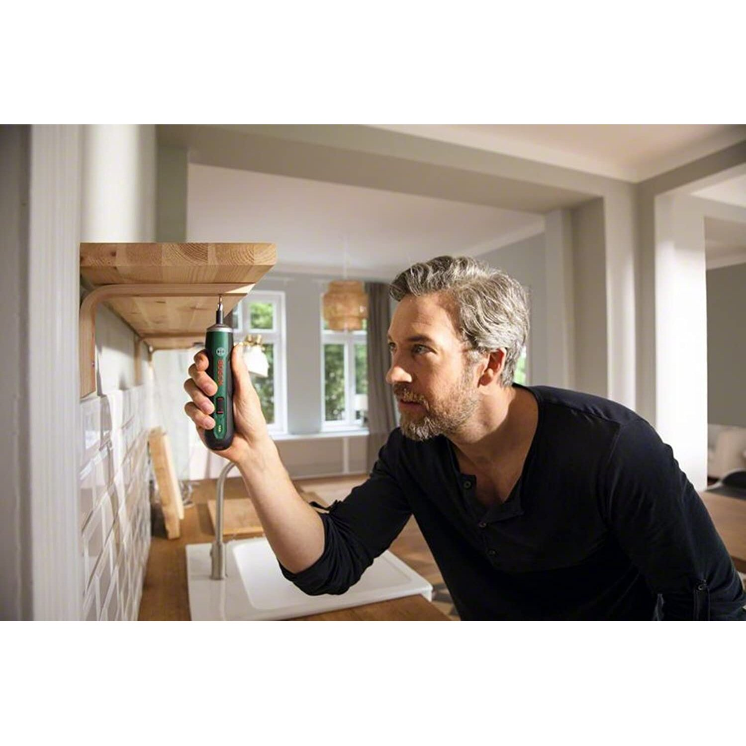 Mężczyzna używający wiertarki na drewnianej półce. Otoczenie kuchenne, neutralne tony.