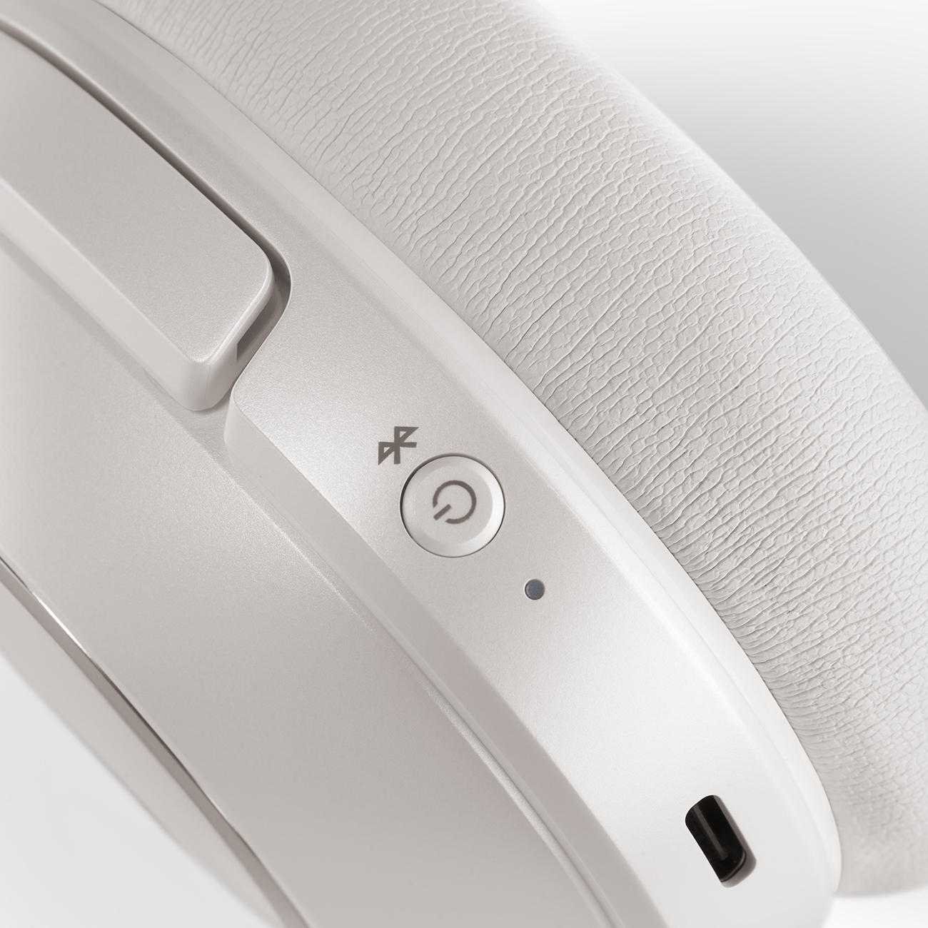 Nahaufnahme weißer Kopfhörer mit Ein-/Aus-Taste und Bluetooth-Symbol.