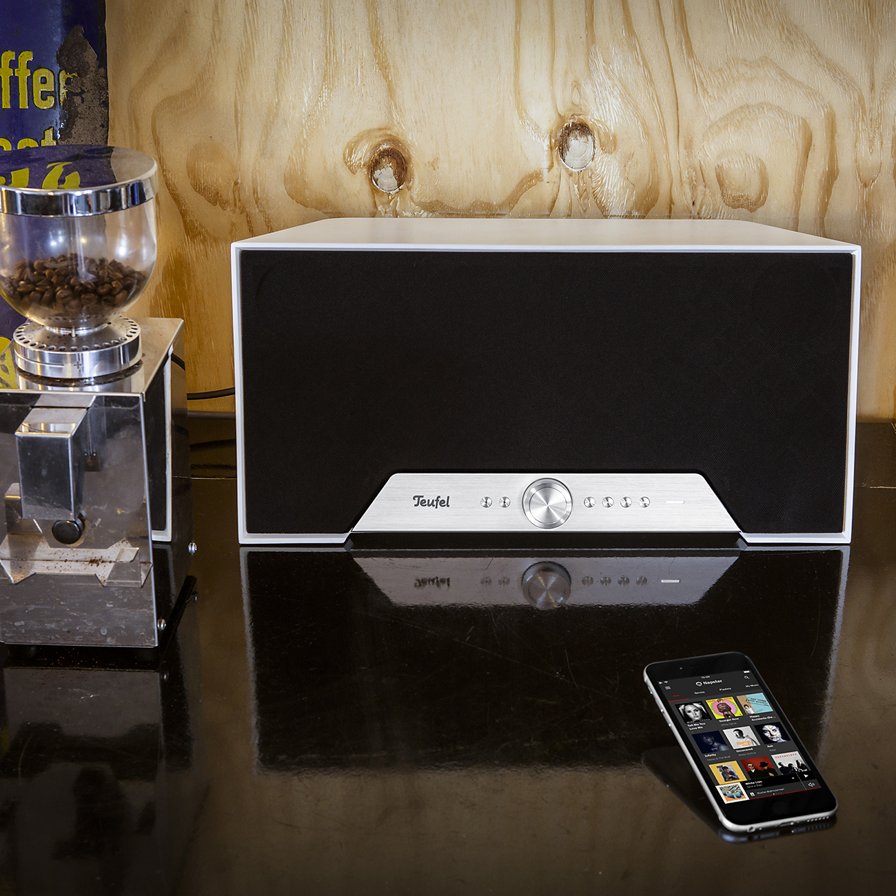Luidspreker op een houten oppervlak naast een koffiemolen en een telefoon.
