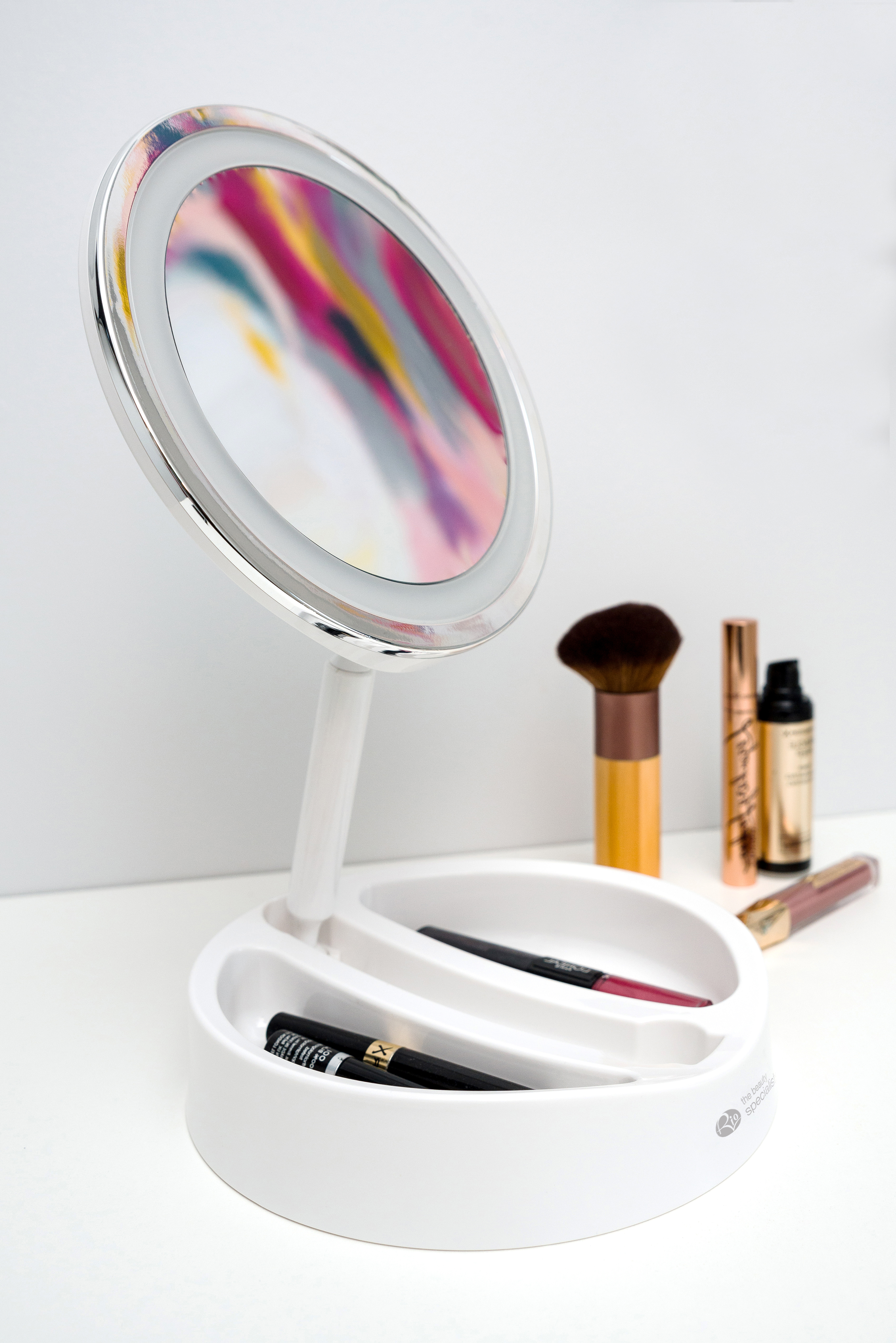 Ein weißer Schminkspiegel mit Make-up-Pinseln und Lippenstiften auf weißer Oberfläche.