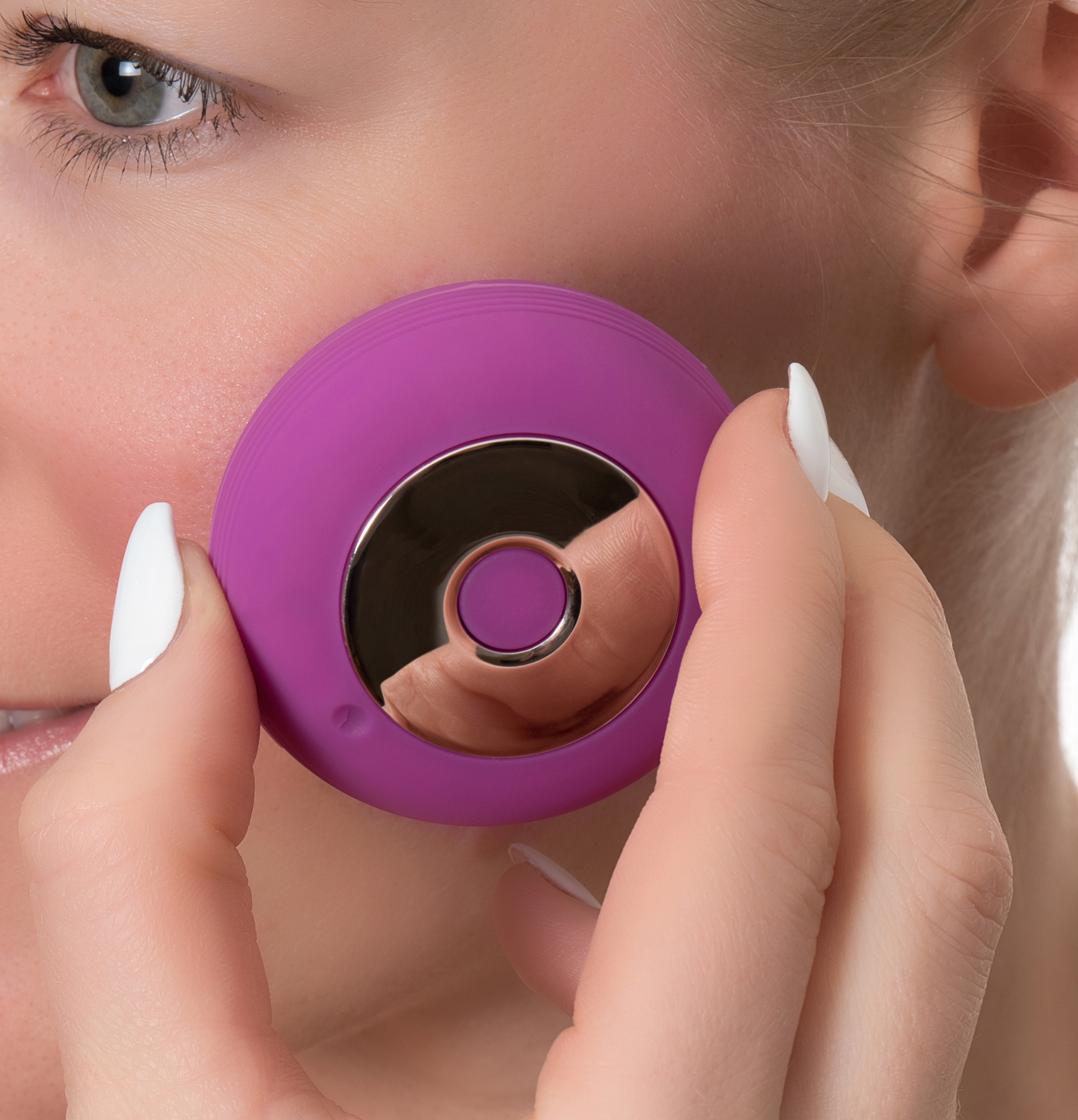 Eine Frau hält ein violettes Gesichtspflegegerät an ihrer Wange.
