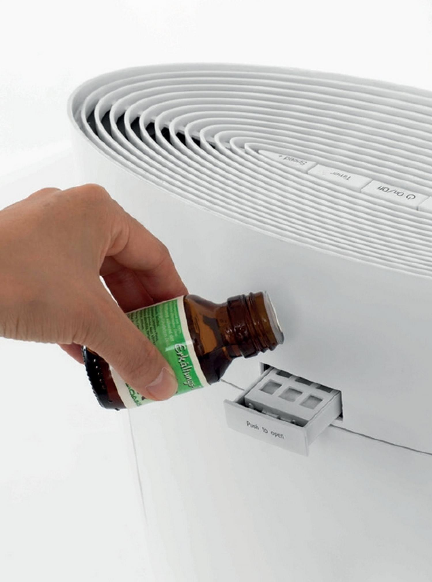 Mano che versa liquido da una bottiglia marrone in un purificatore d'aria bianco. Vicino al vassoio aperto.