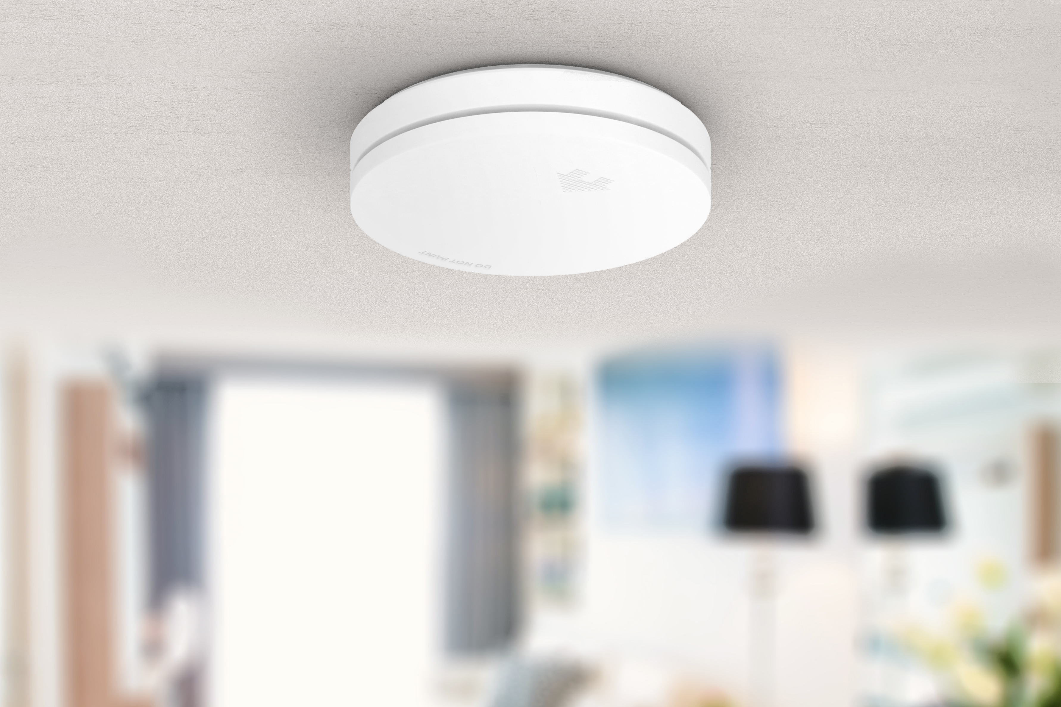 Rilevatore di fumo rotondo bianco su un soffitto bianco. Interno con sfondo sfocato di una stanza.