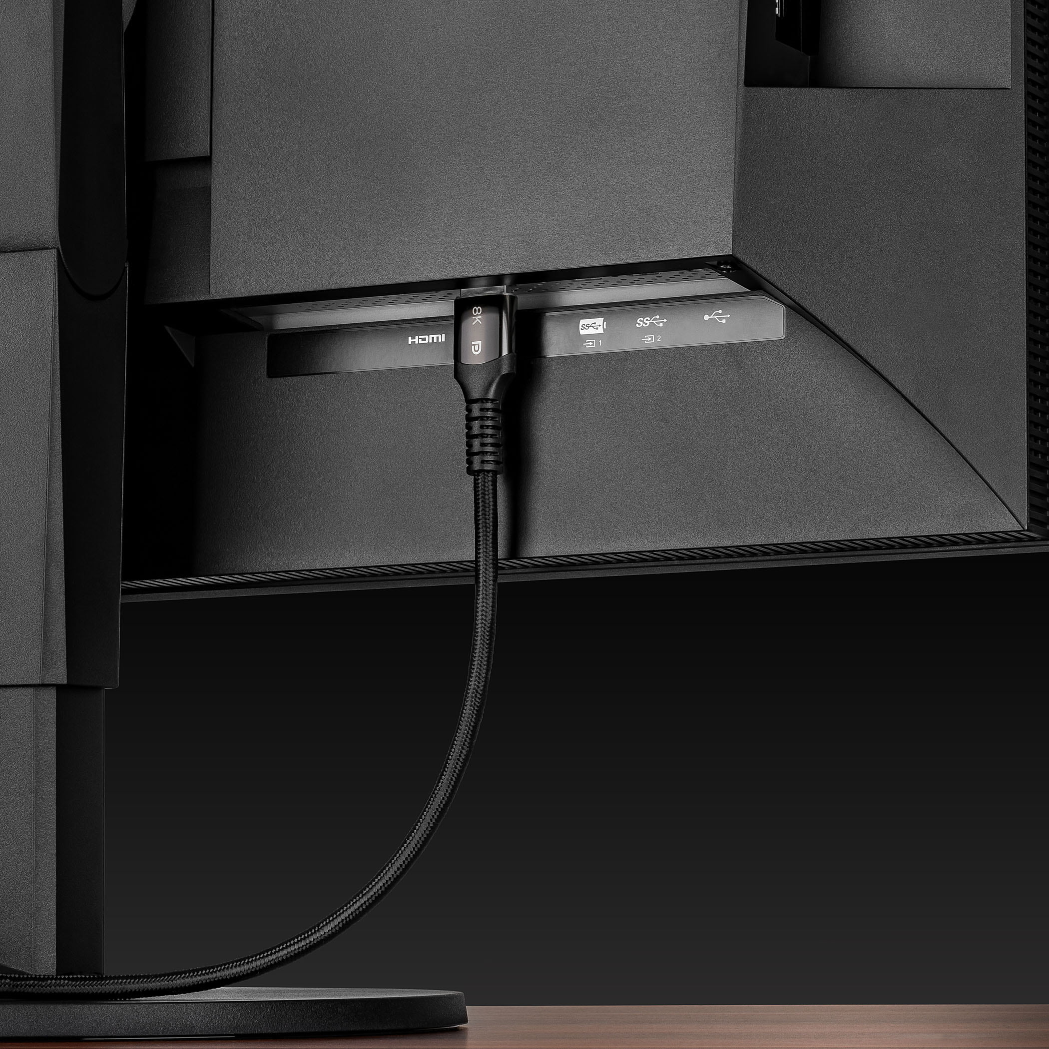 Die Rückseite eines schwarzen Monitors mit HDMI- und USB-Anschlüssen ist sichtbar, ein Kabel ist angeschlossen.