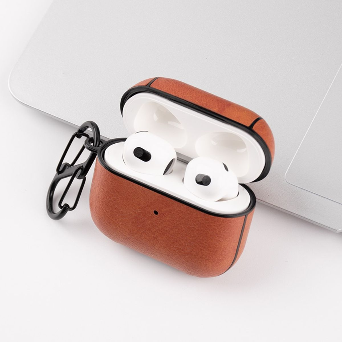 Geöffnete braune Leder-AirPods-Hülle mit weißen AirPods darin. Auf einem Laptop platziert.